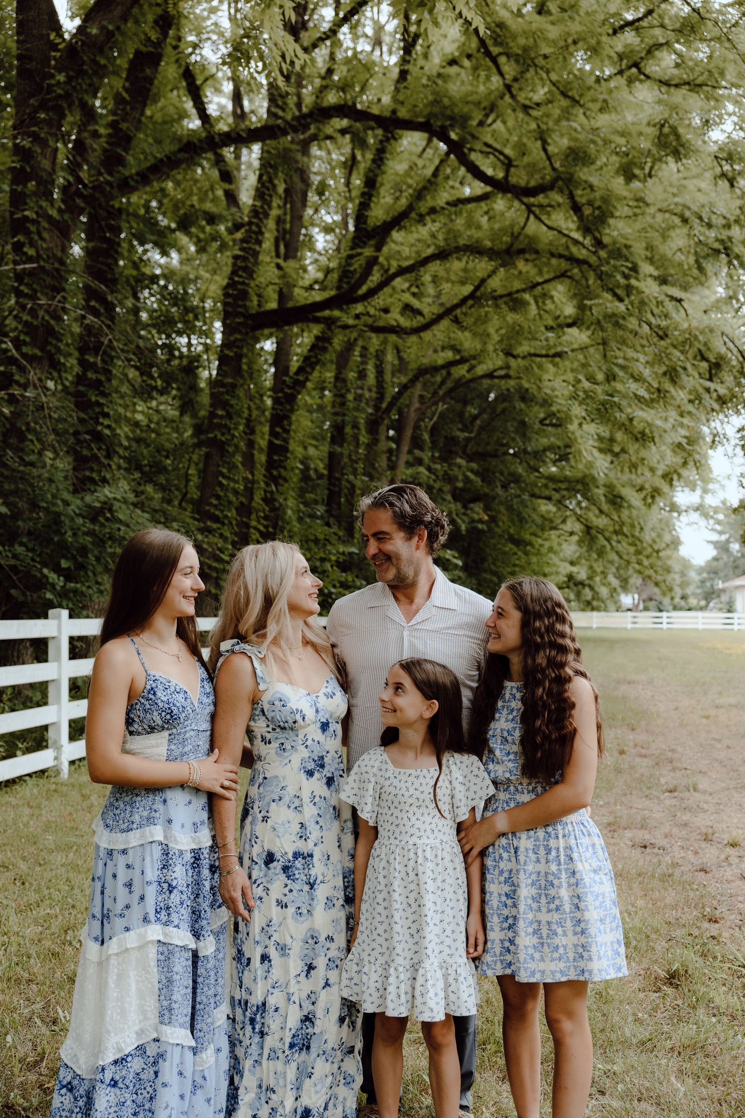 Group wearing coordinated blue and white floral dresses posing together by a white fence.