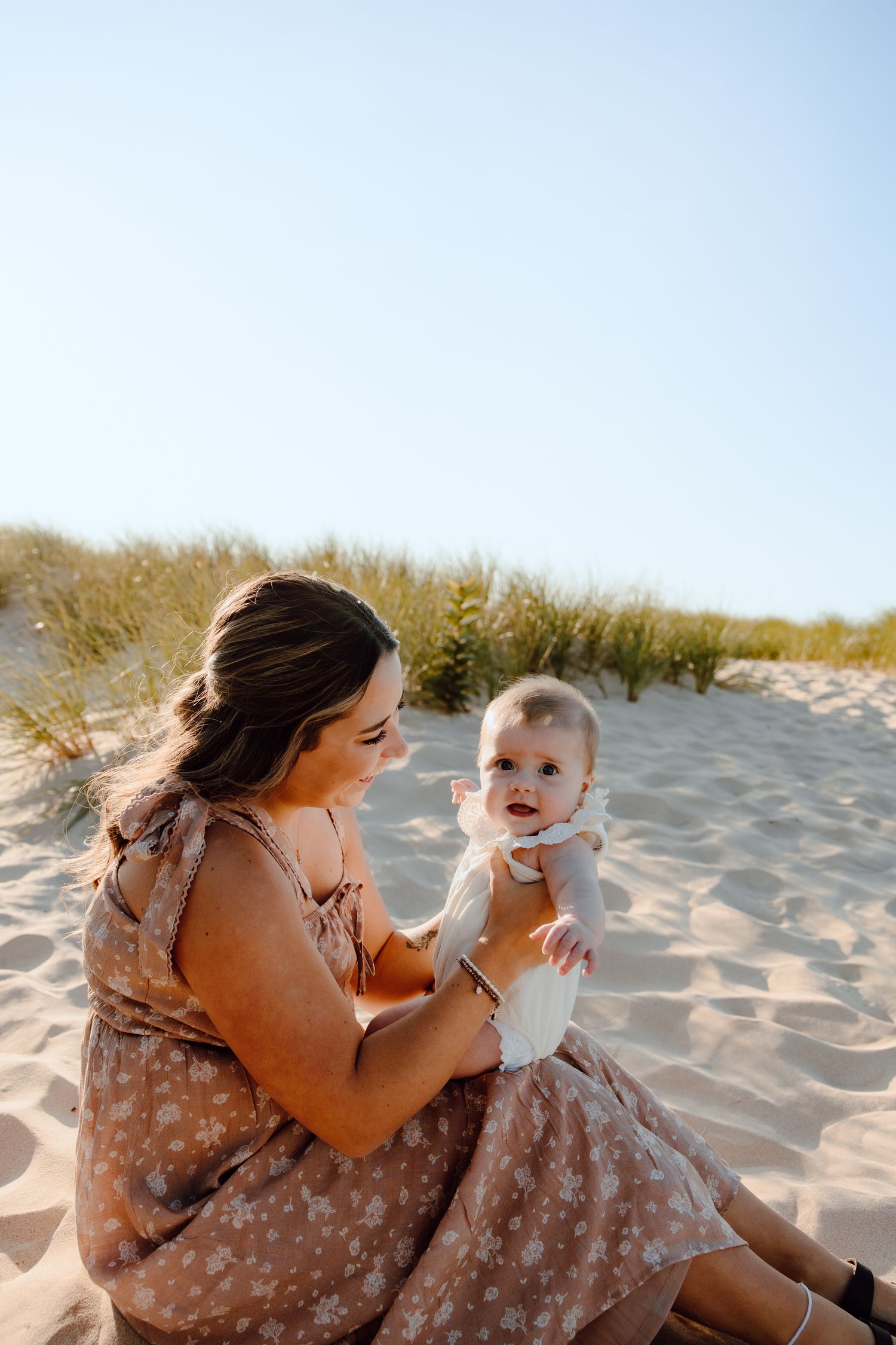 A tender moment between parent and child sitting in sandy dunes at sunset.