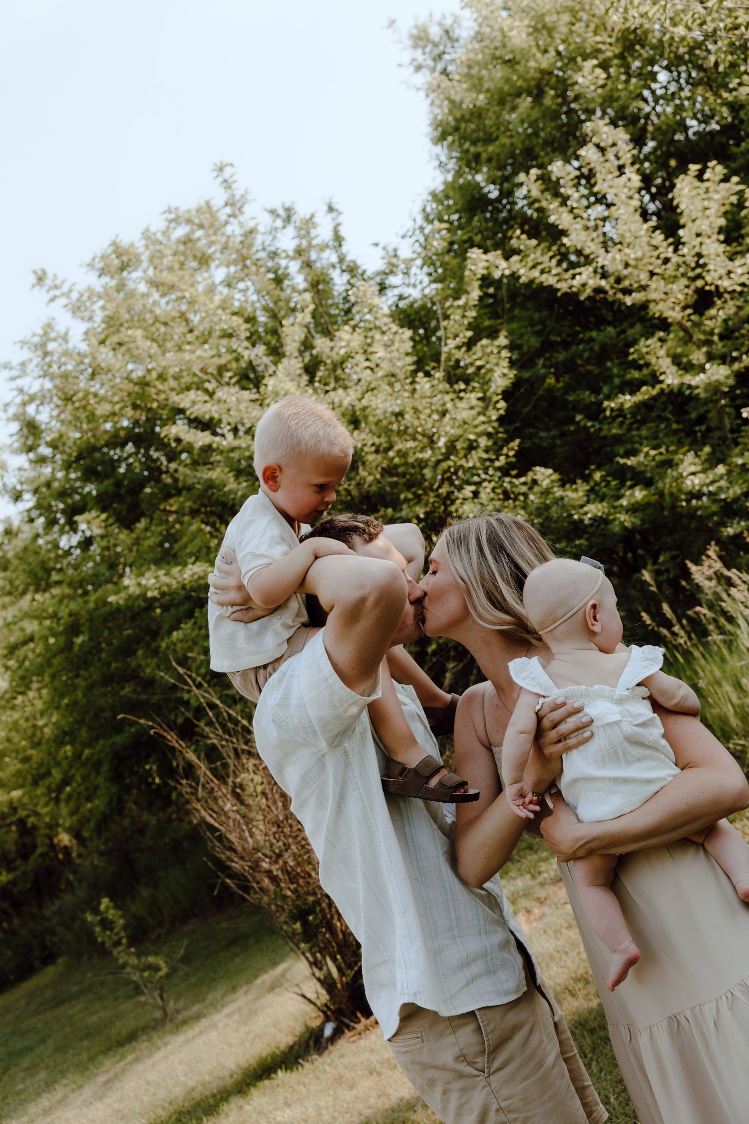 A joyful family moment captured outdoors with parents lifting their children in a playful pose.