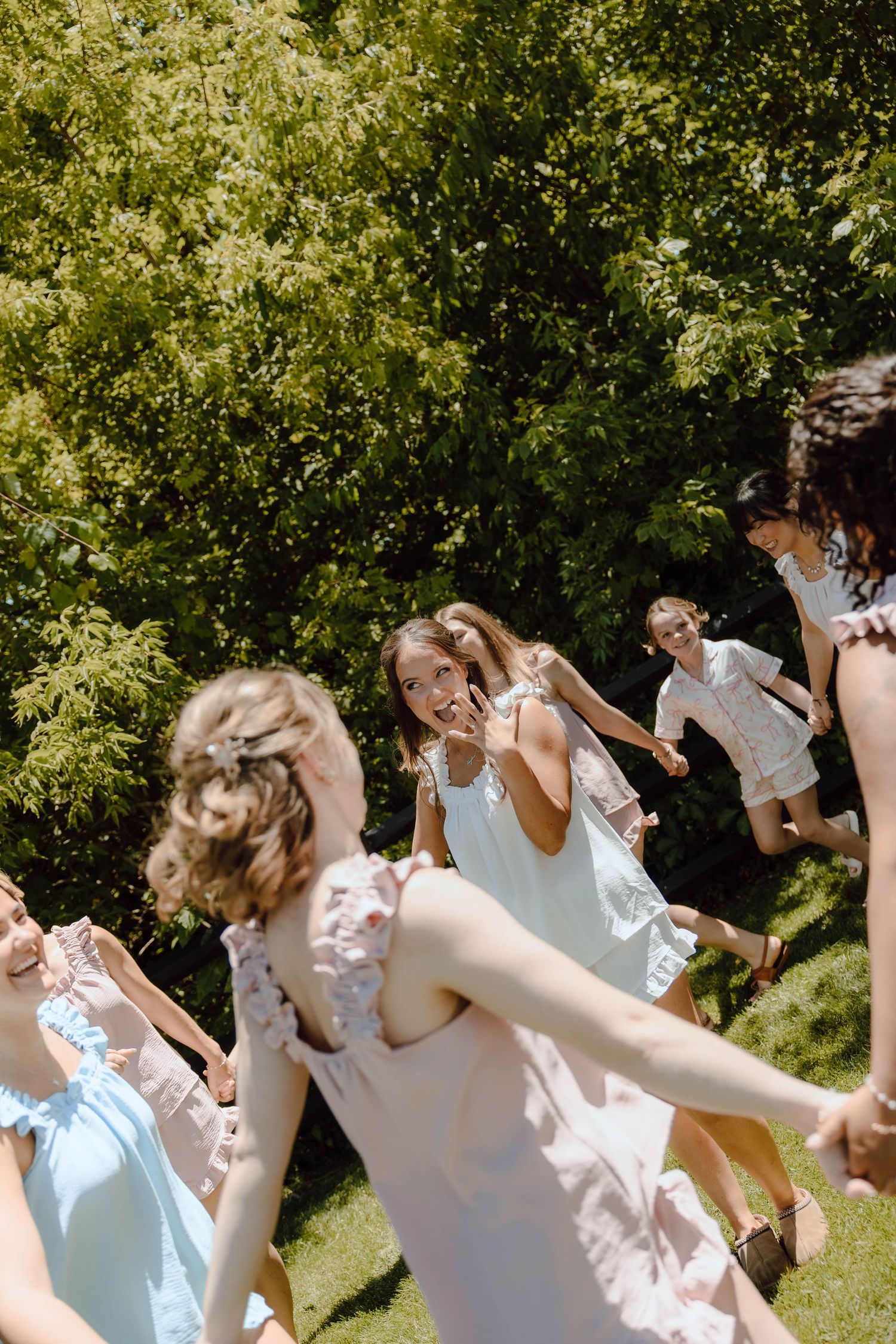 Young women in summer dresses dancing and playing outdoors in a sunny green garden, one flashing a peace sign.