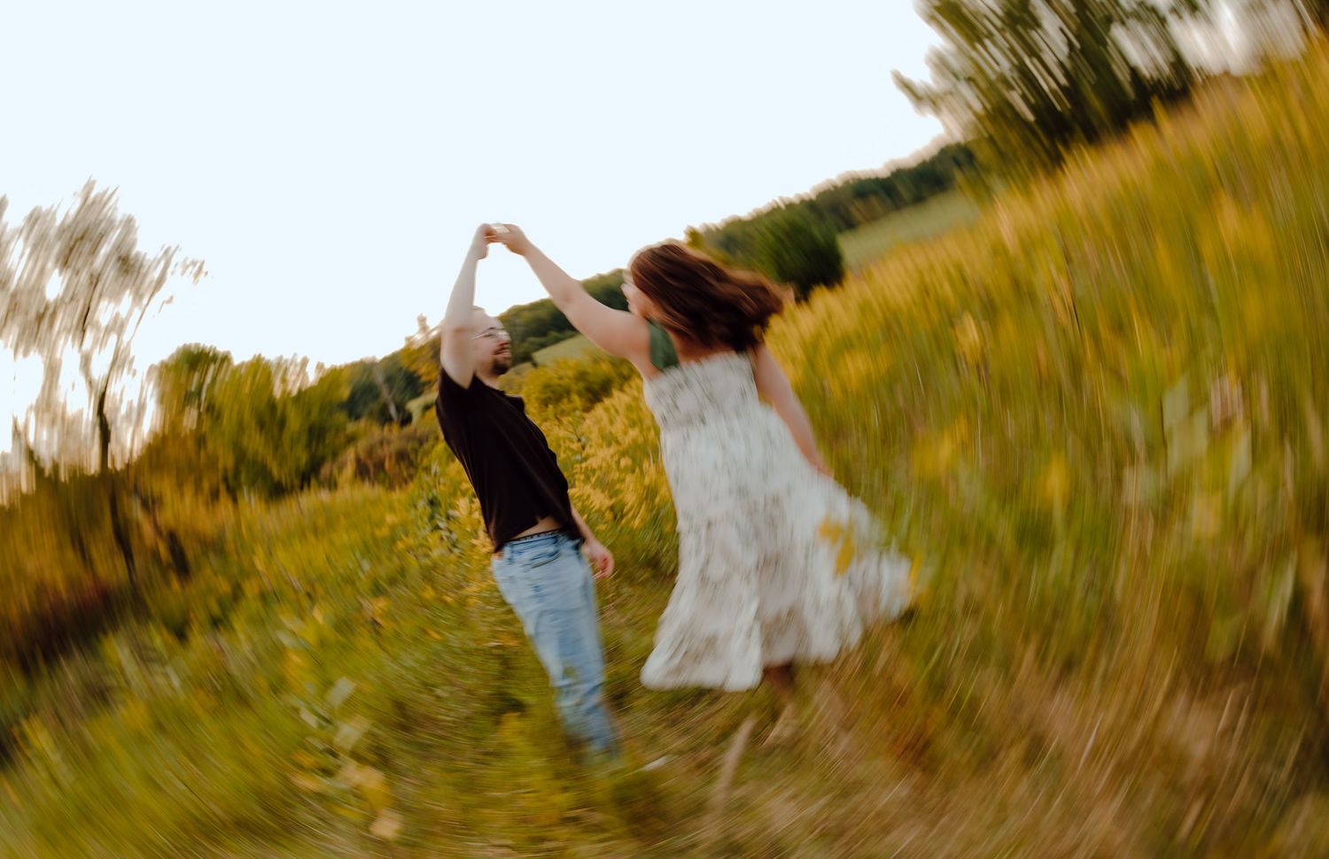 Motion-blurred photo of a couple spinning in a golden field at sunset.