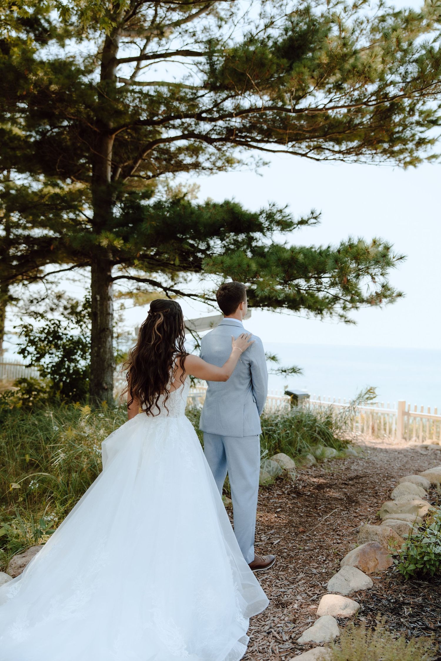 Bride and groom walk toward ocean view through pine trees on their wedding day.
