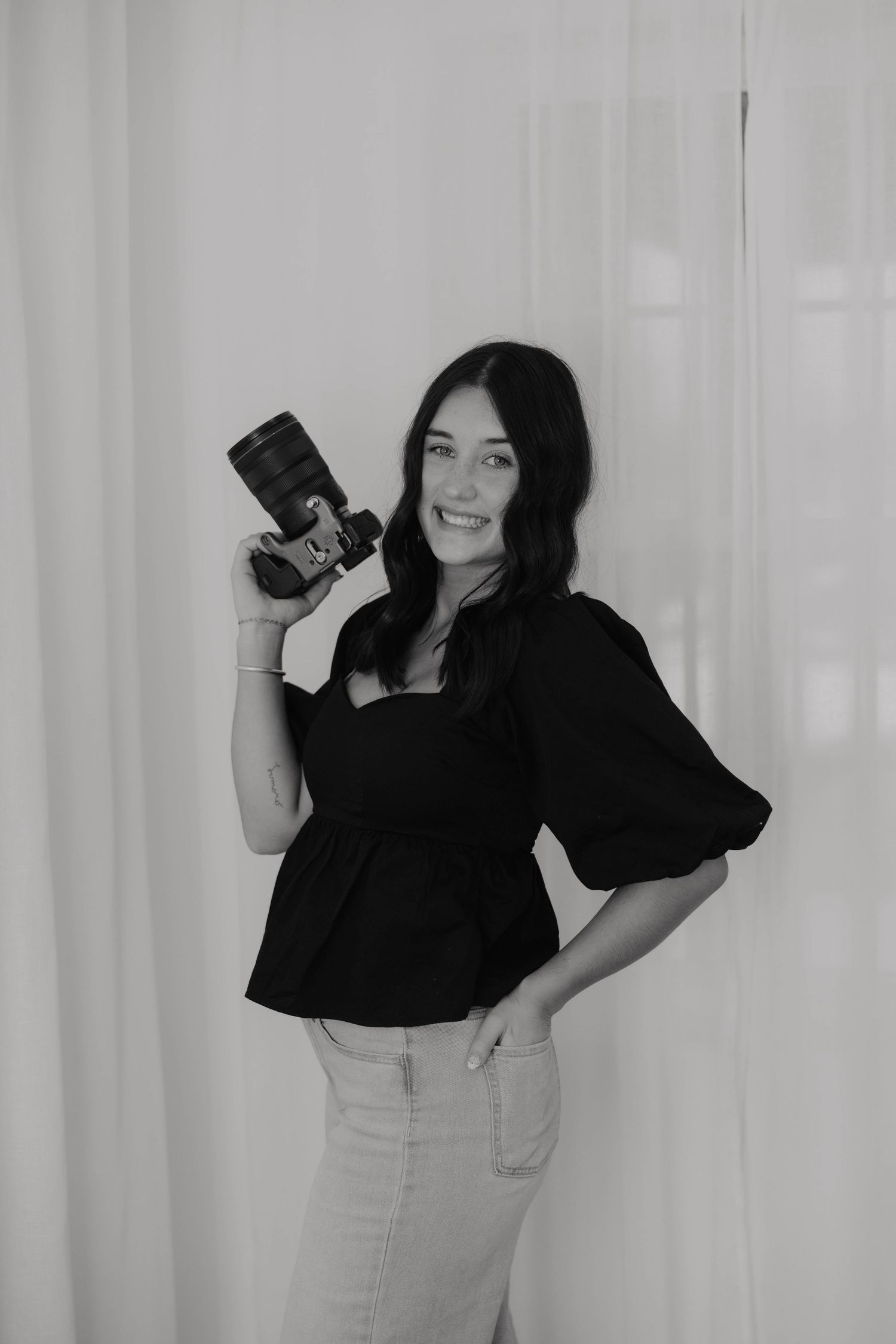Professional photographer poses with camera in black and white studio portraits.