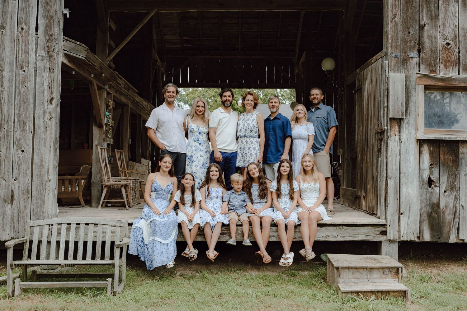 Wide group portrait in front of weathered barn with everyone wearing coordinated outfits.