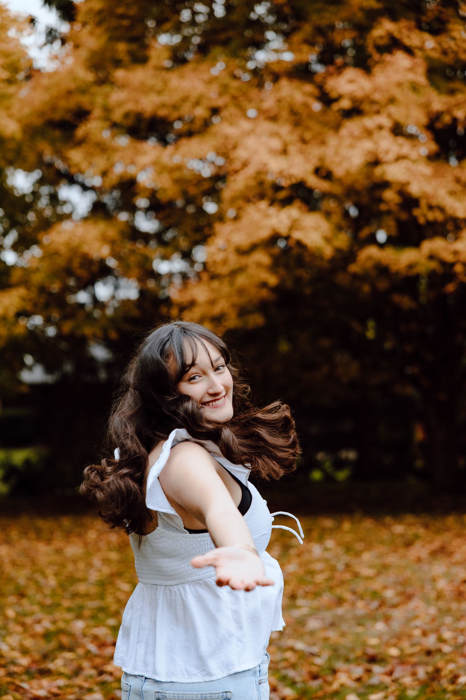 Carefree movements captured in a white dress during a fall photo session with golden foliage.