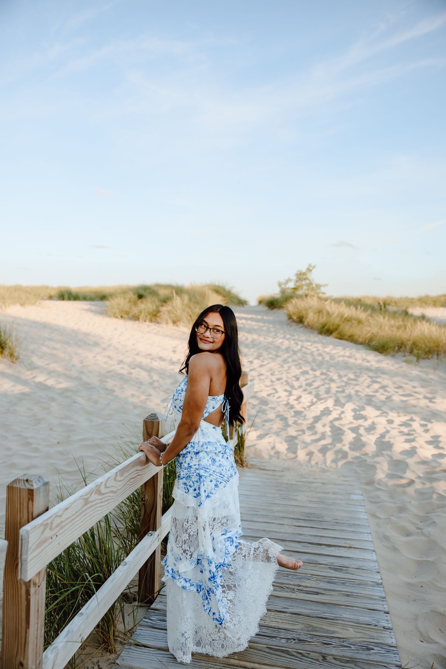 A blue and white dress flows elegantly along a wooden boardwalk at the beach.