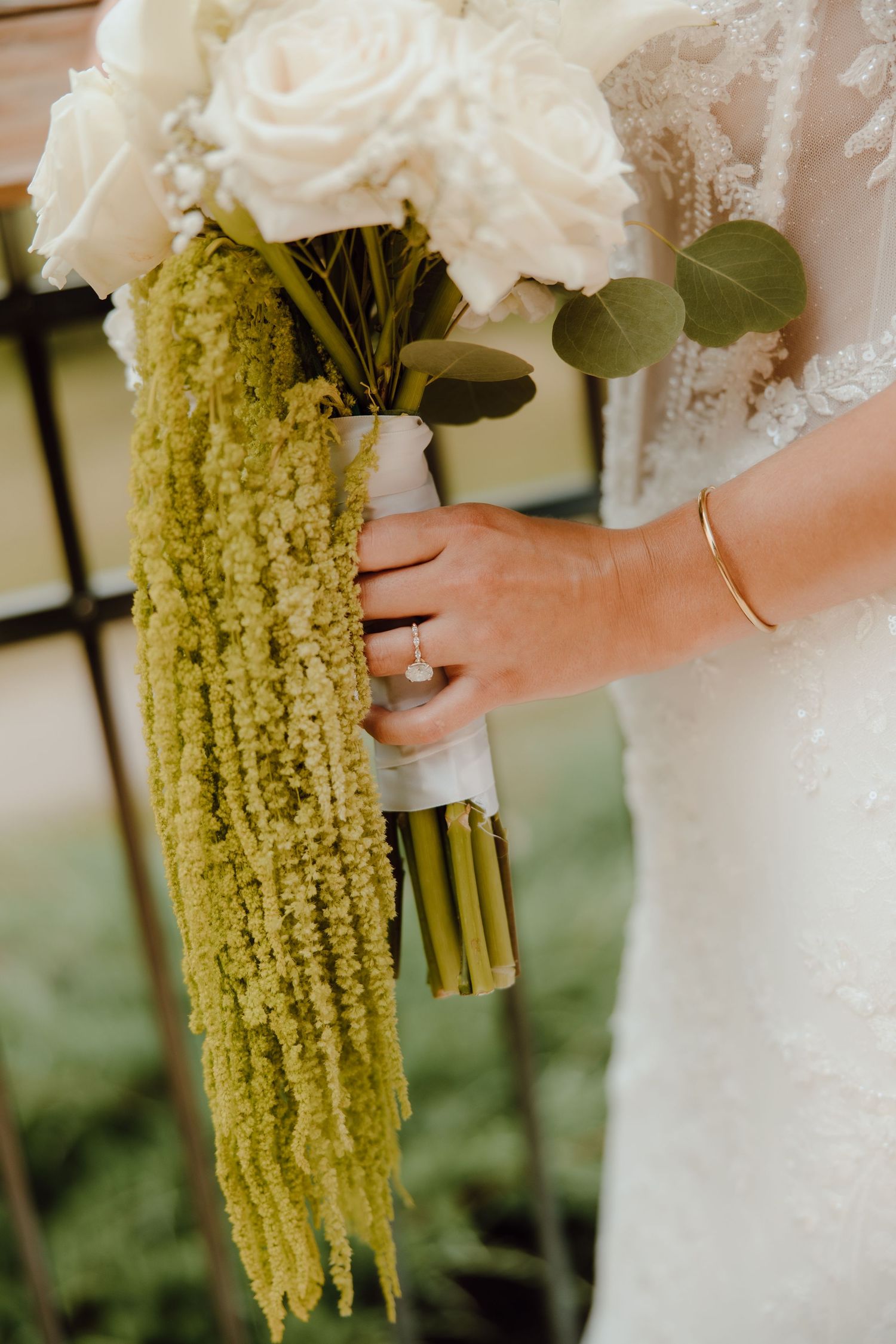 Bride holding a wedding bouquet of white roses and cascading green amaranthus, wrapped in white ribbon.