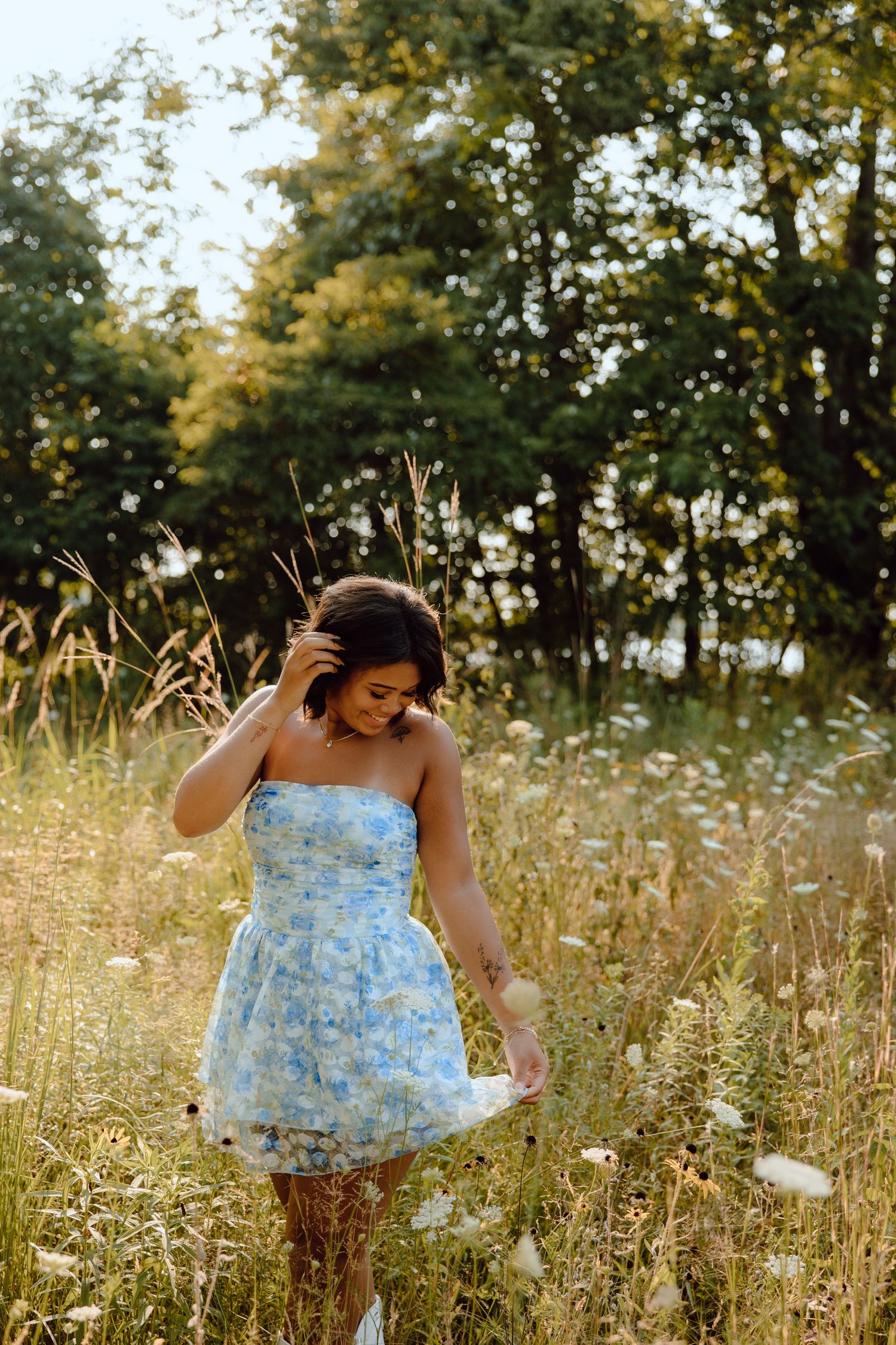 Playful summer photoshoot in a blue floral dress among tall wildflowers.
