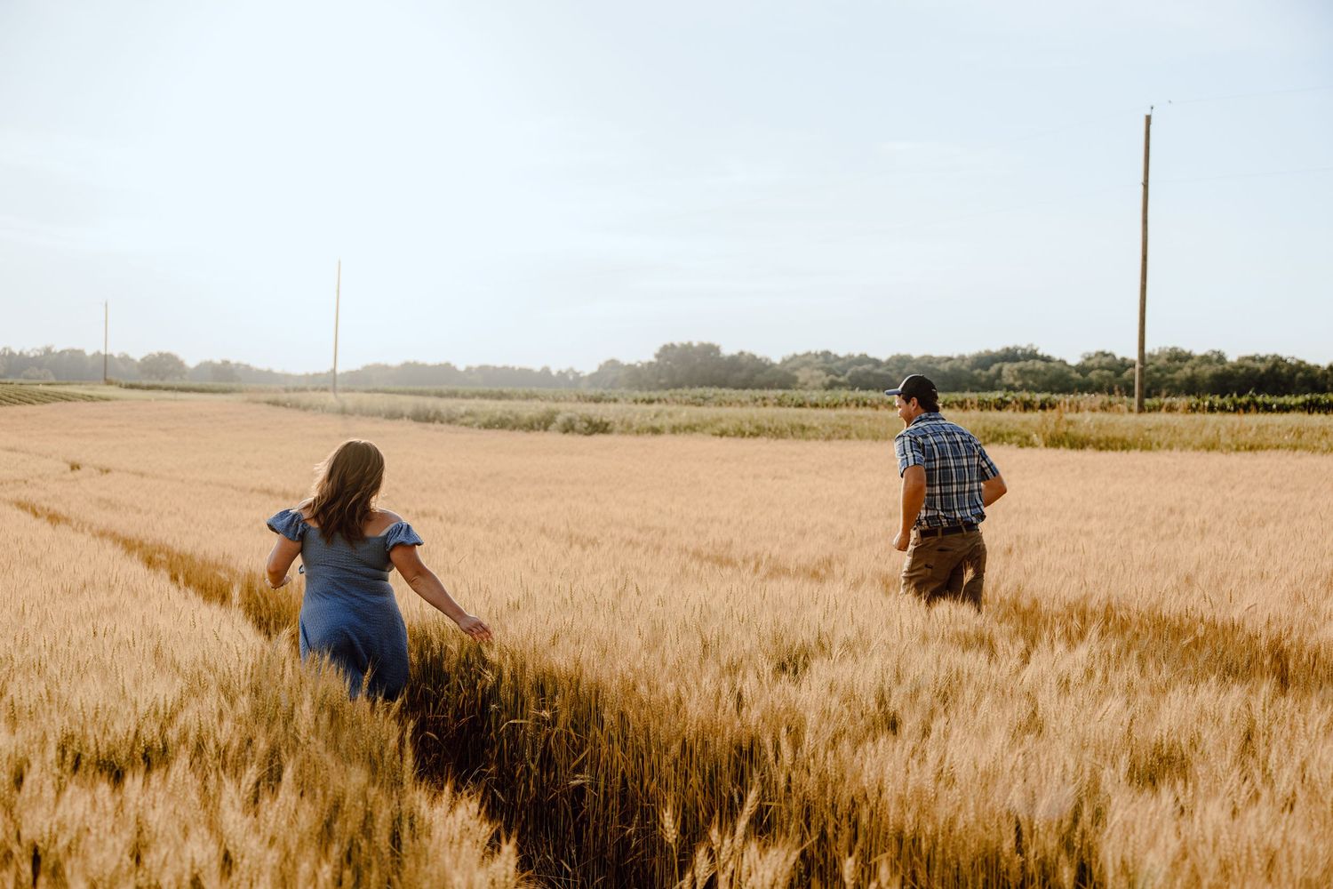 A couple walks through a vast golden wheat field on a sunny day.