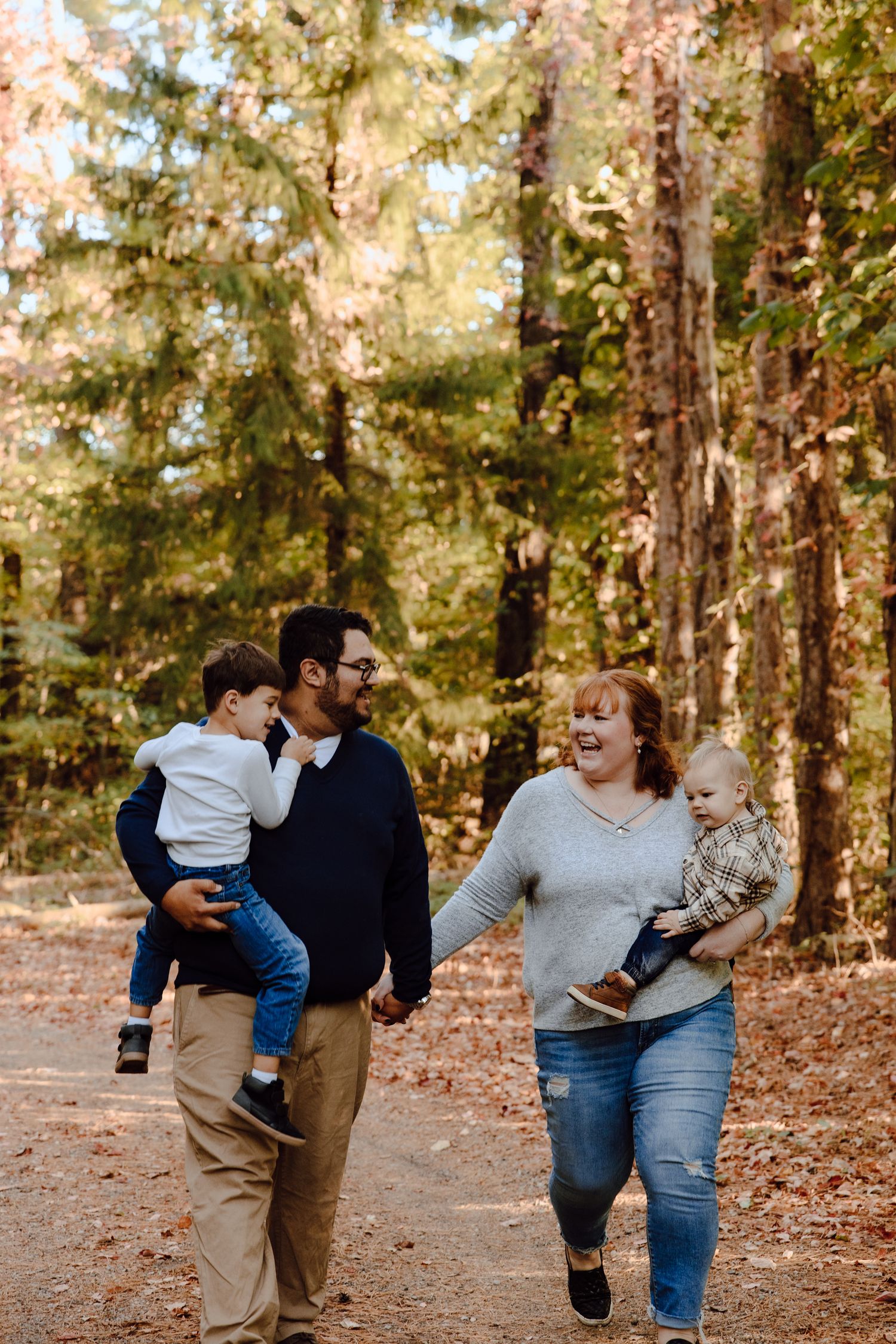 Family plays and interacts playfully in a wooded autumn setting.