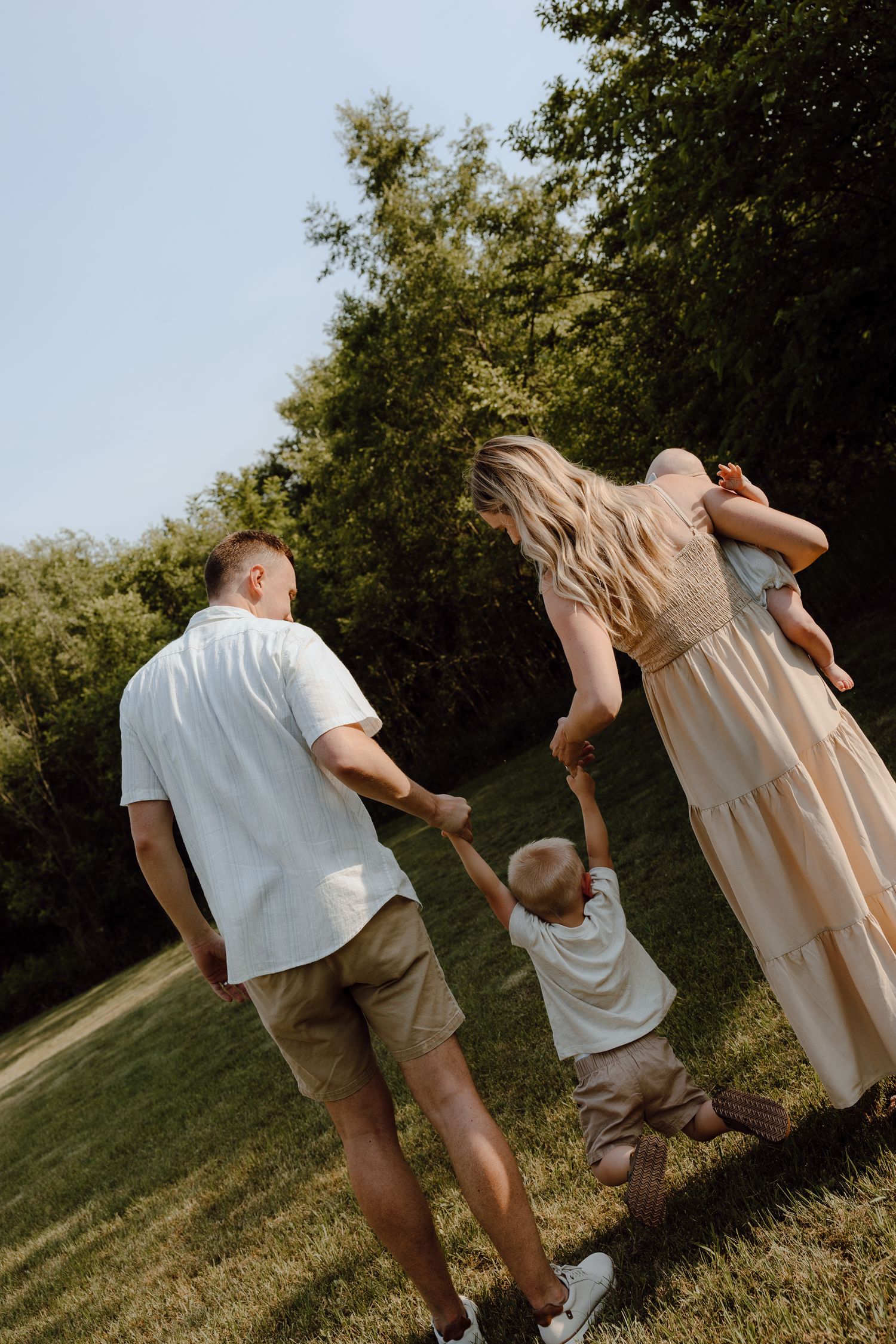 Candid sequence of parents playing and spinning with their child on a grassy hillside at sunset.
