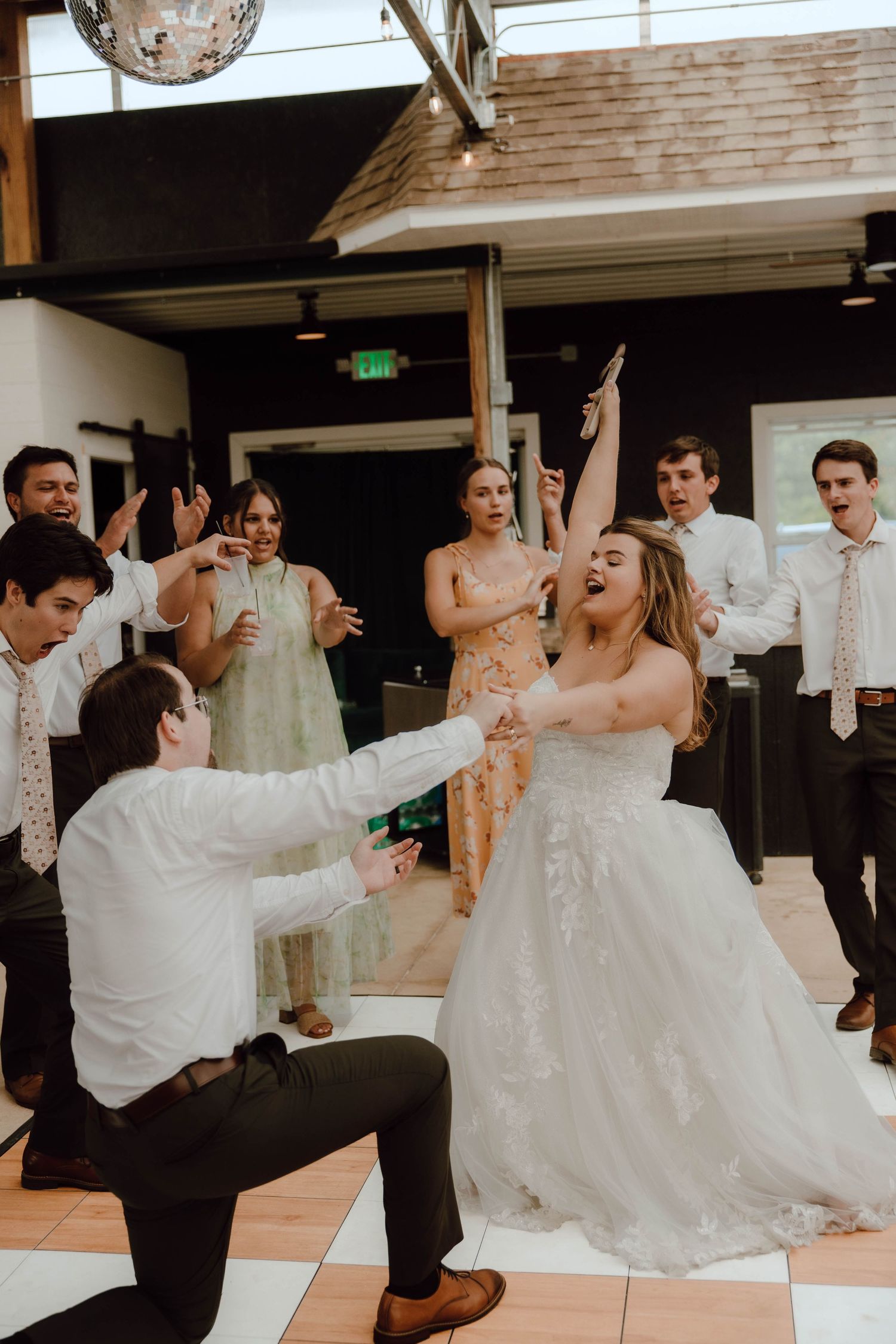 Bride dancing joyfully with wedding guests on checkered dance floor during lively reception celebration.
