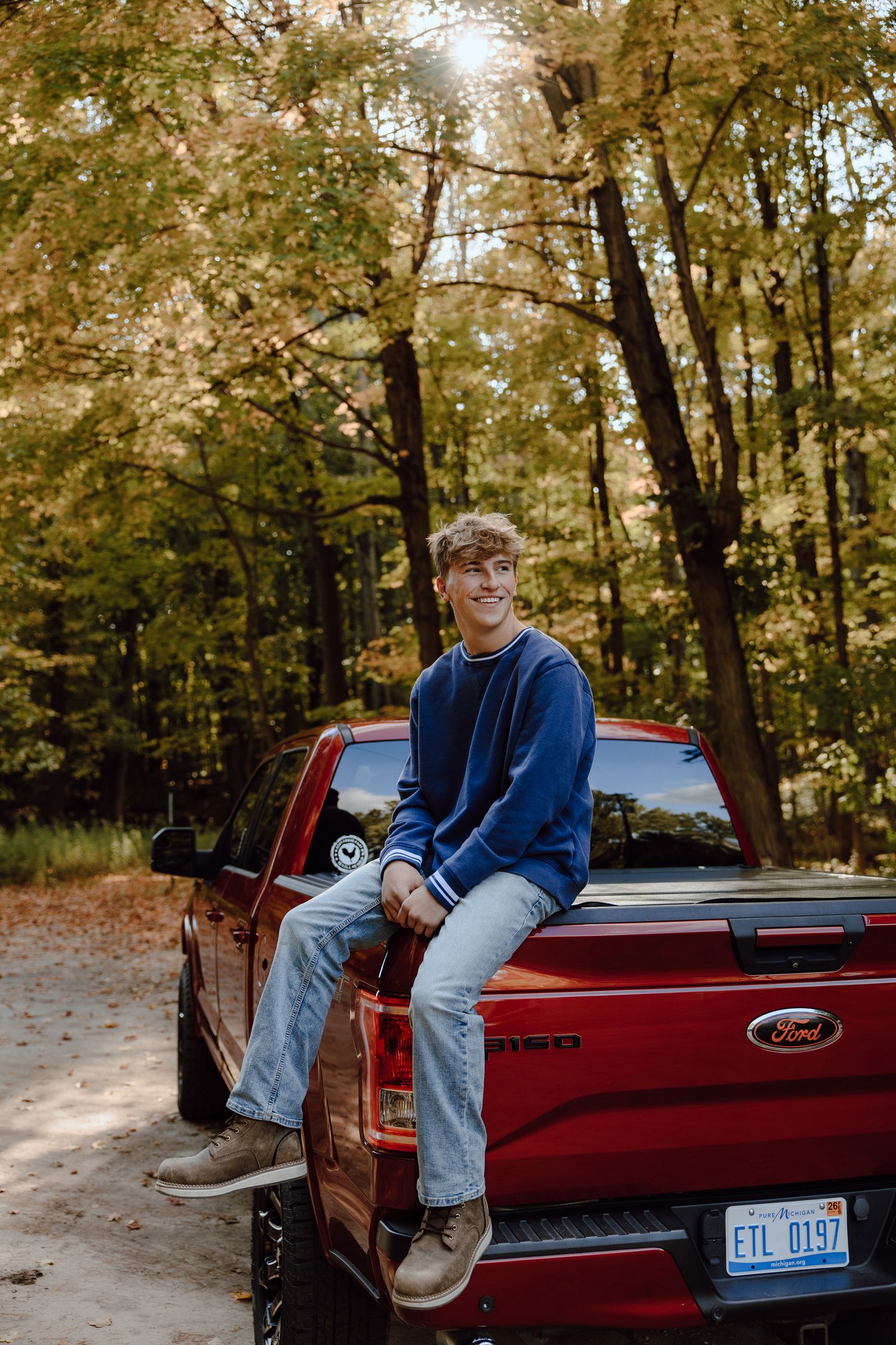 Person sitting on the edge of a red Ford pickup truck bed in a forest setting.