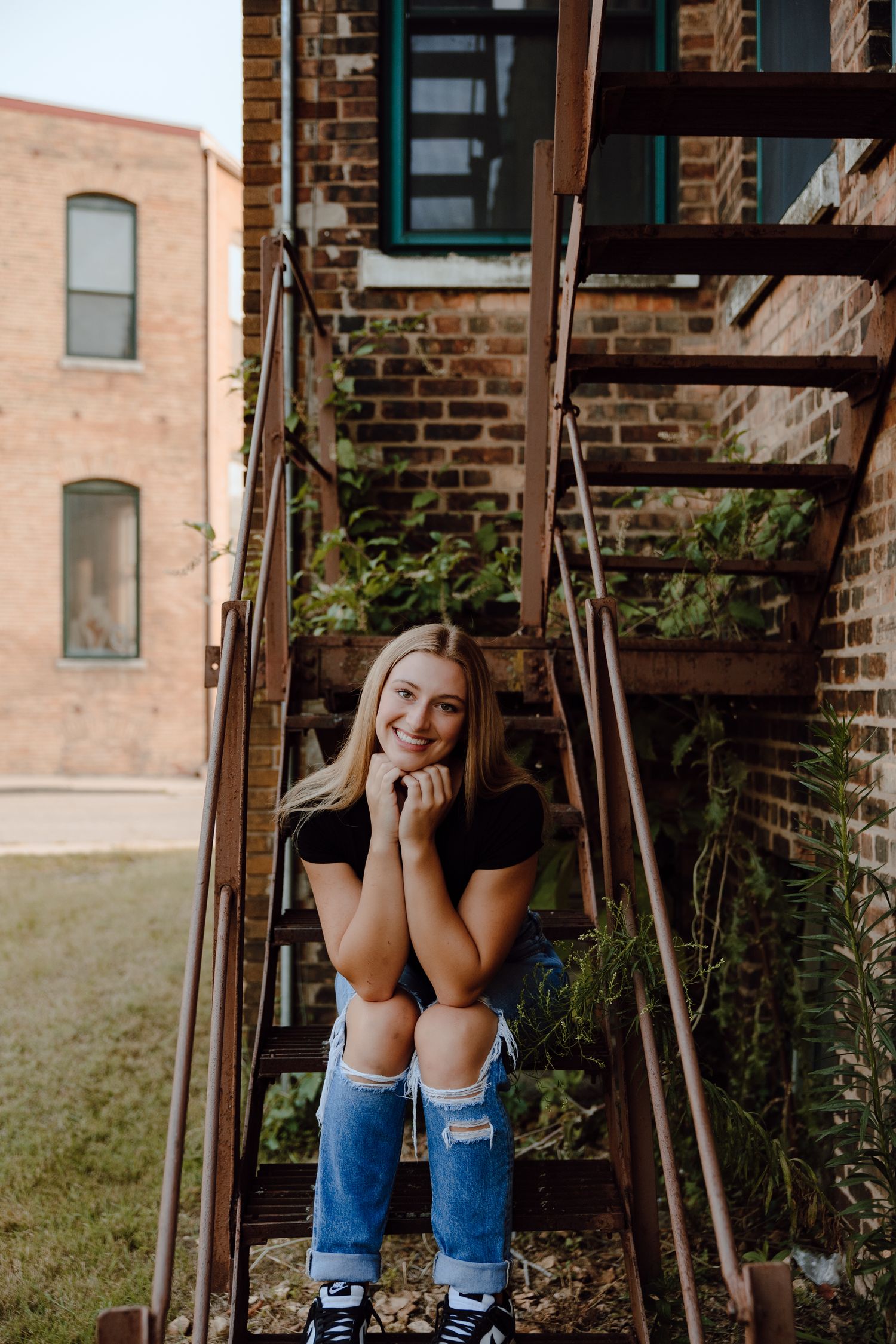Person sitting casually on wooden swing against brick building backdrop.