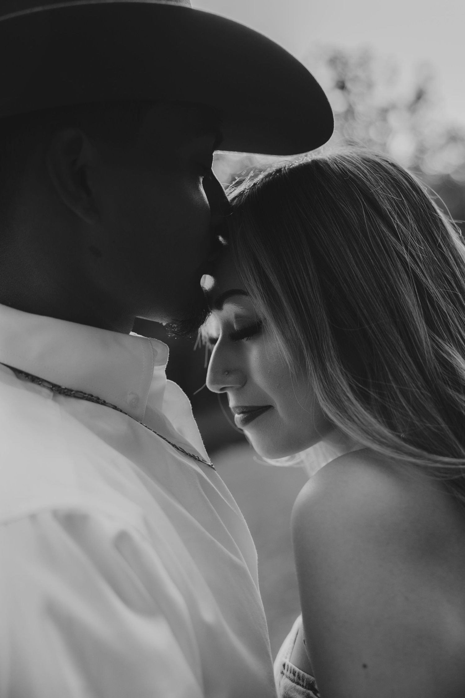 Intimate black and white portrait of couple in western attire sharing a tender moment.