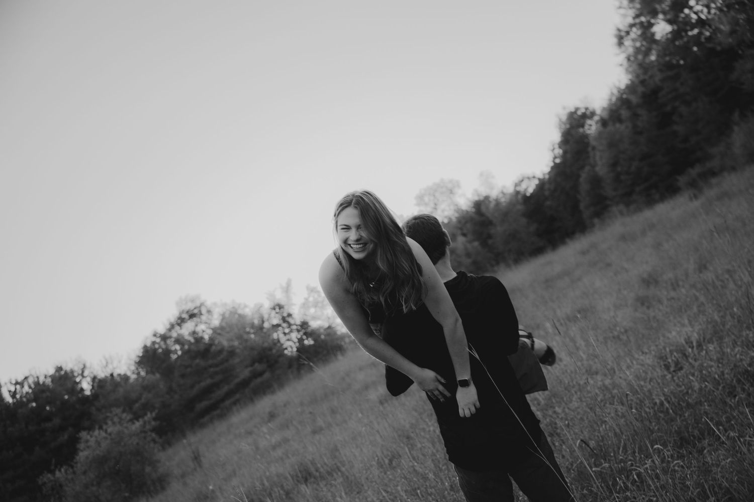 Black and white image of playful couple having fun on a hillside.