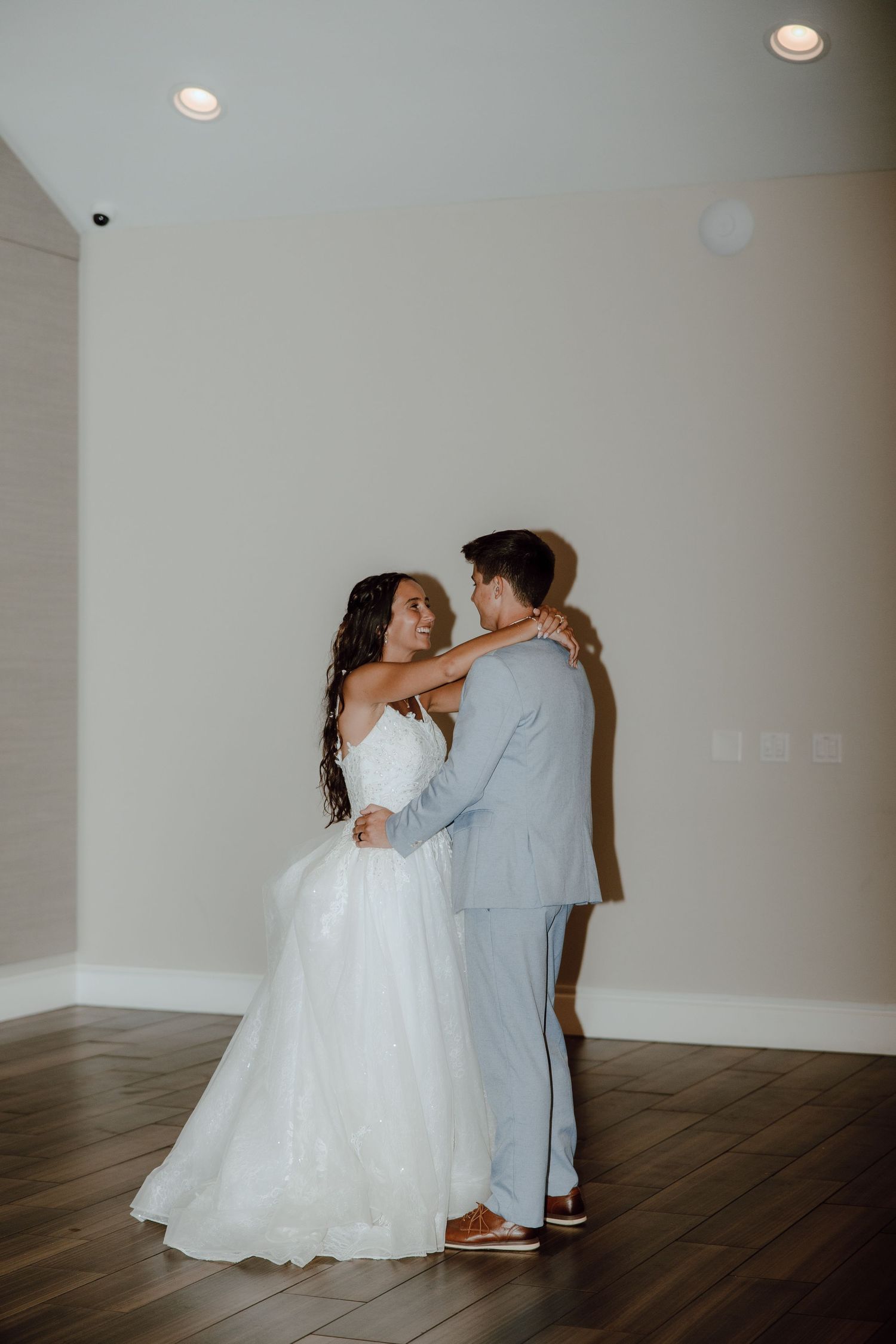Bride and groom sharing first dance in softly lit modern venue, groom in light blue suit.