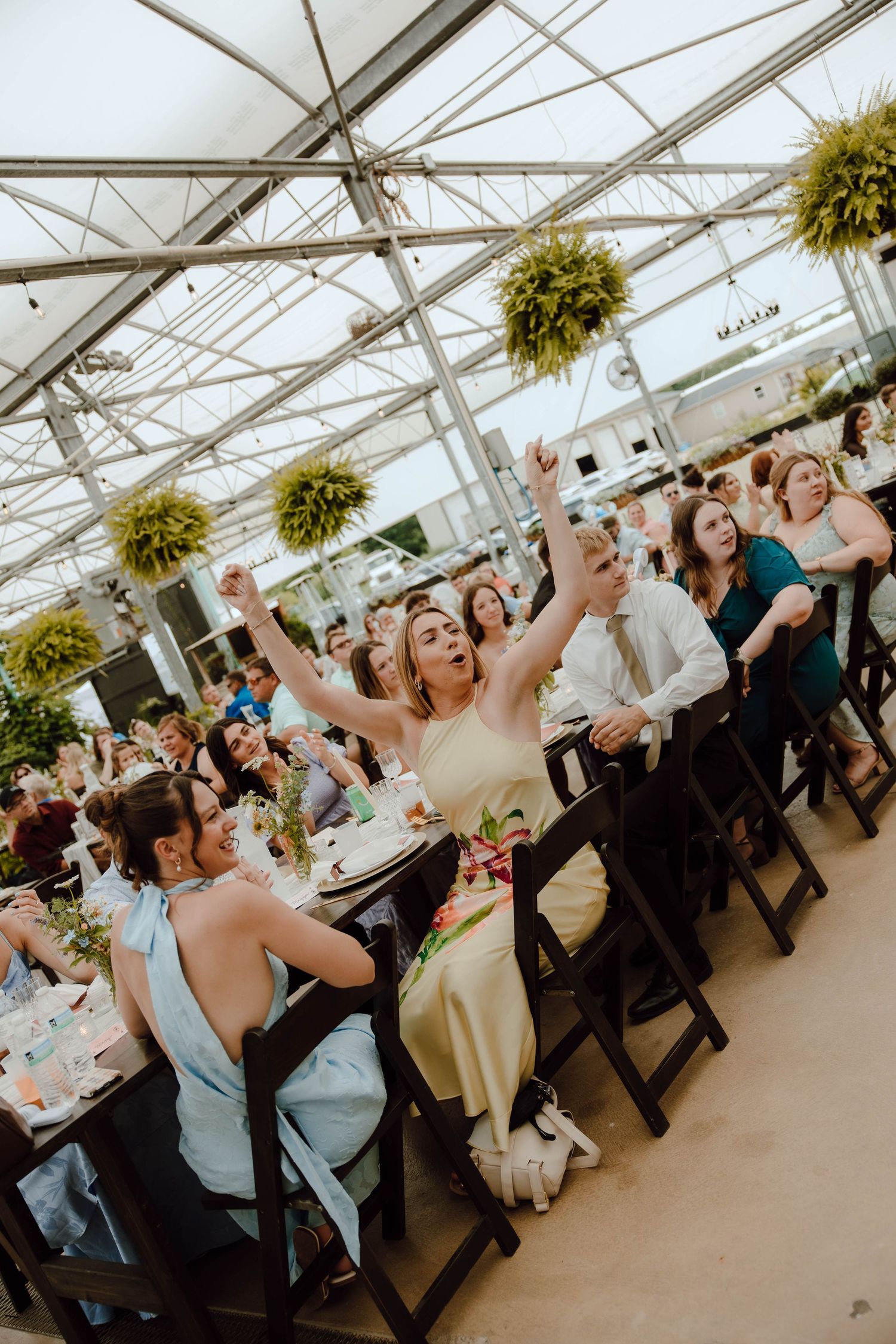 Wedding reception guests celebrating in a greenhouse venue with hanging plants.
