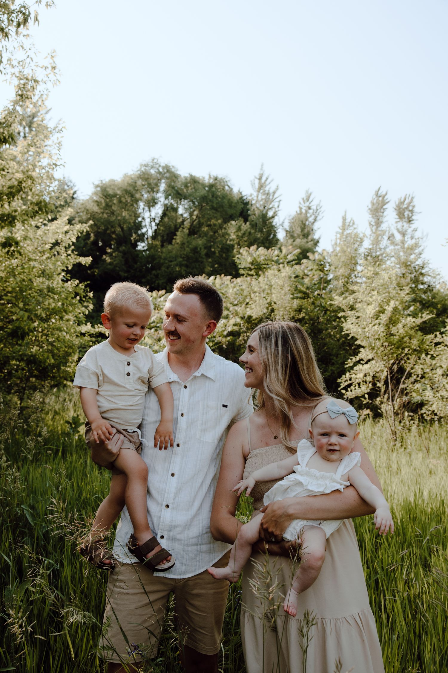 Family portrait in tall grass with natural lighting and greenery backdrop.
