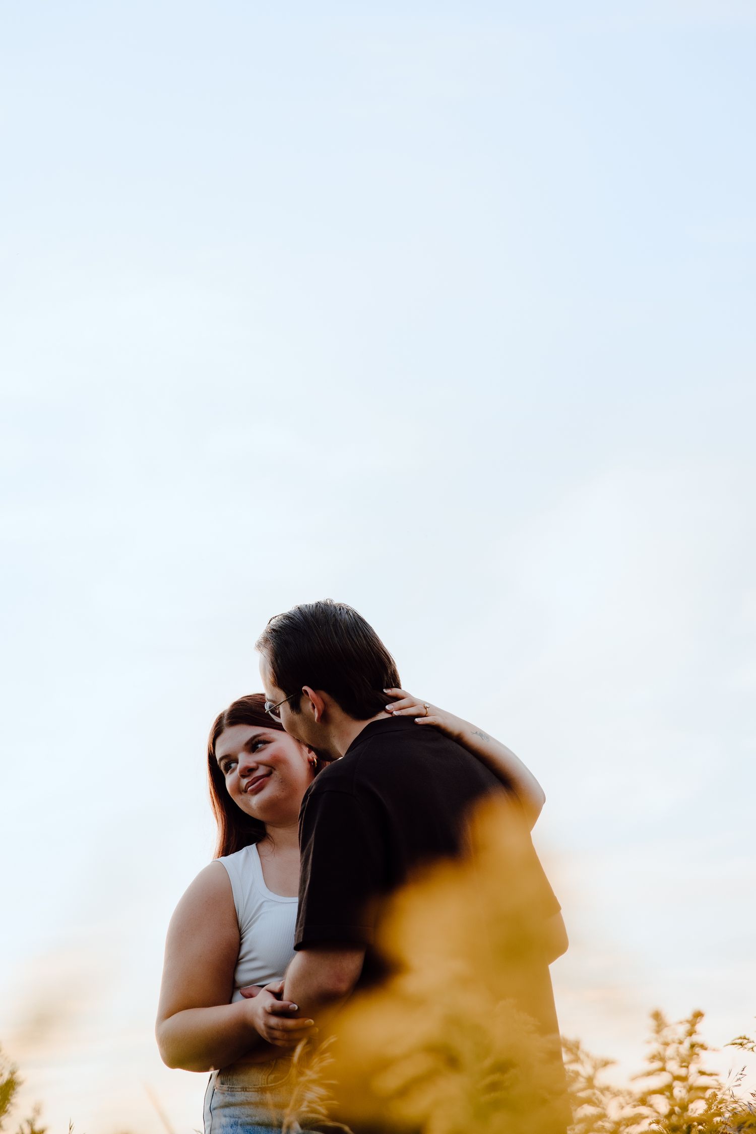 Silhouetted figures embrace against a bright sky during golden hour.
