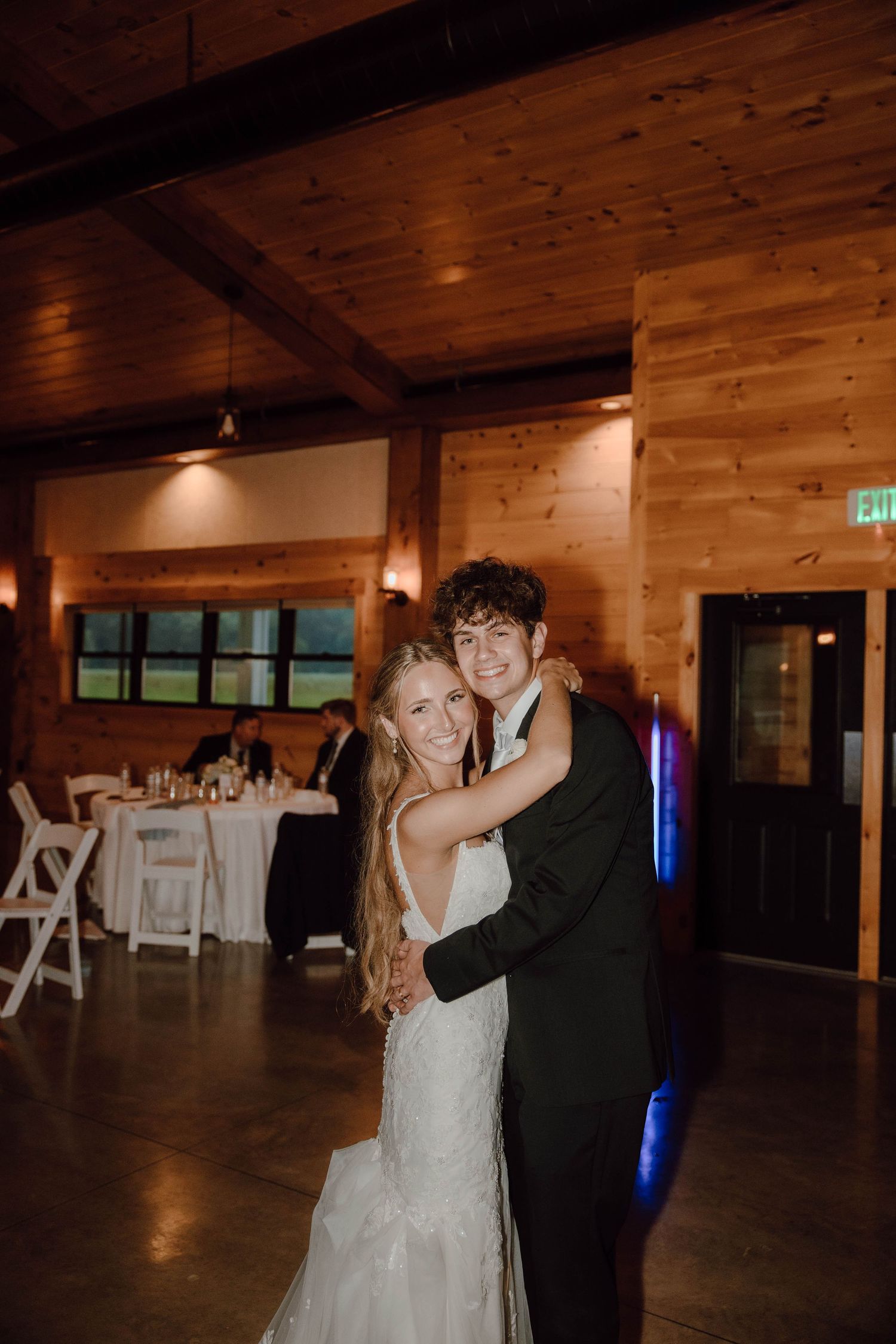 Smiling bride and groom share a romantic first dance in a warmly lit rustic barn venue.