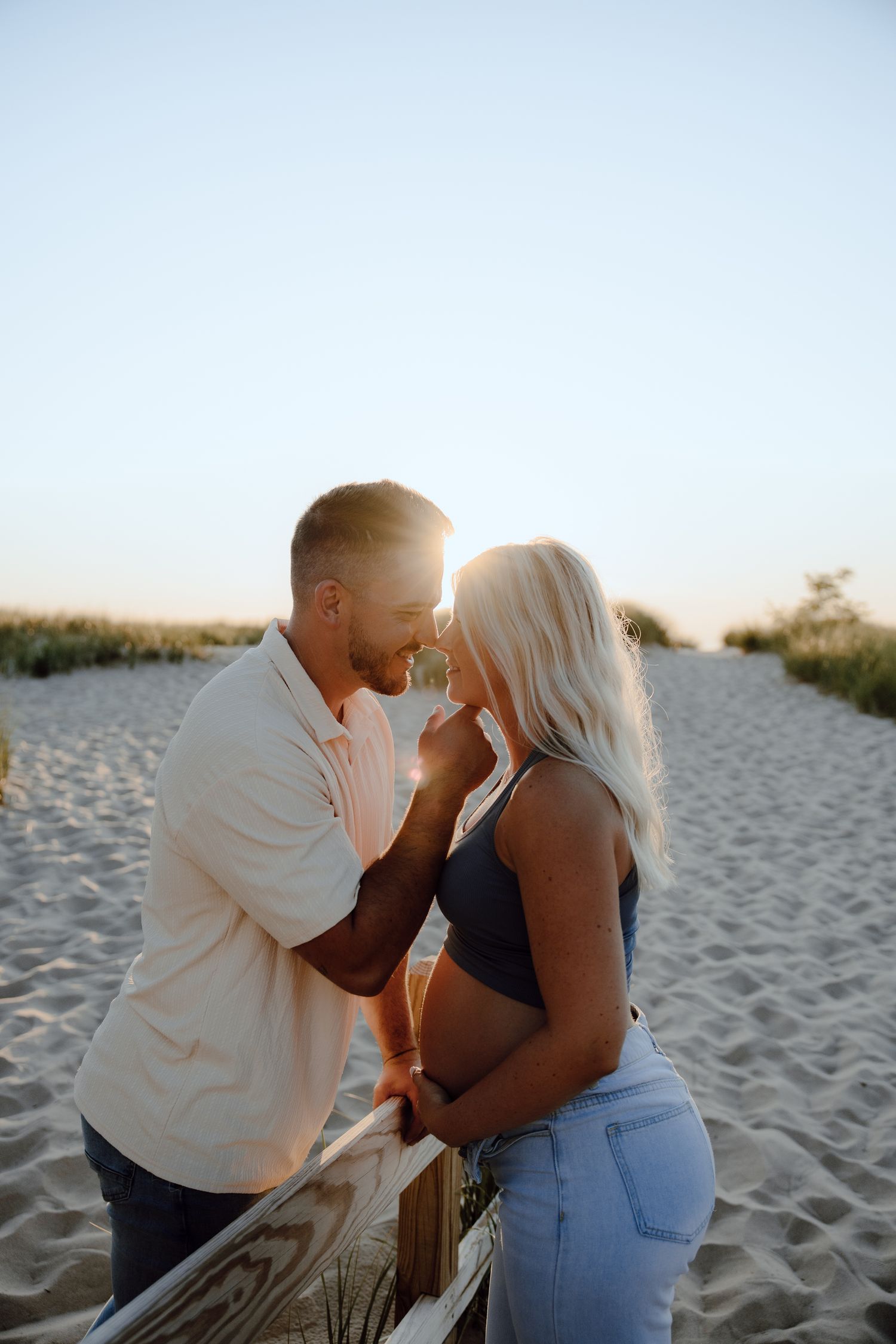 A romantic sunset photoshoot on a sandy beach with warm golden light filtering through the scene.