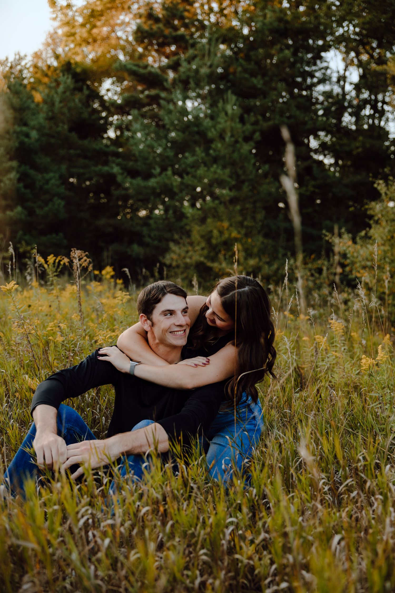 A couple lounges in tall grass during a romantic outdoor photo session.