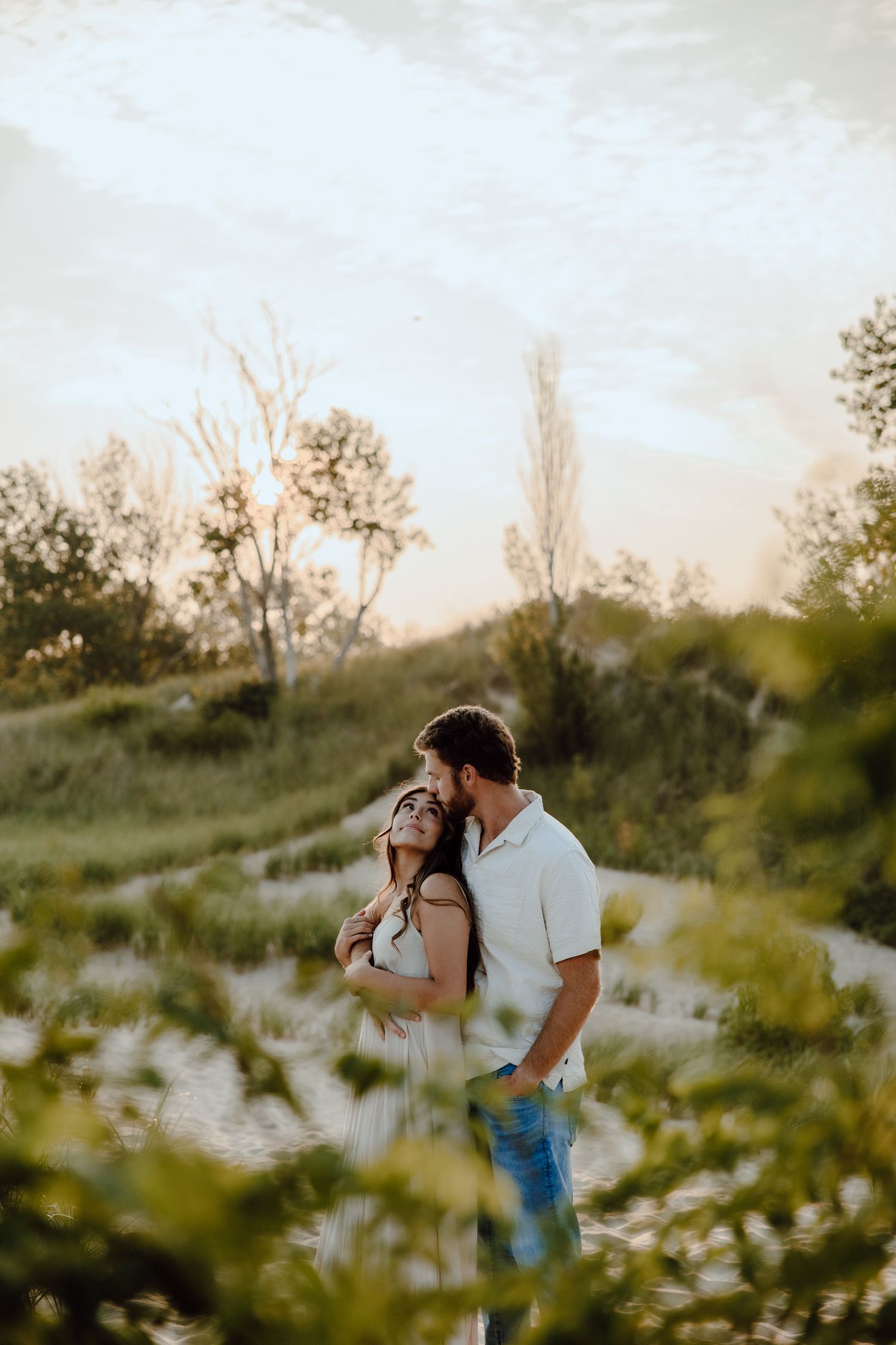 Romantic couple embracing in a natural setting with golden sunlight filtering through trees.