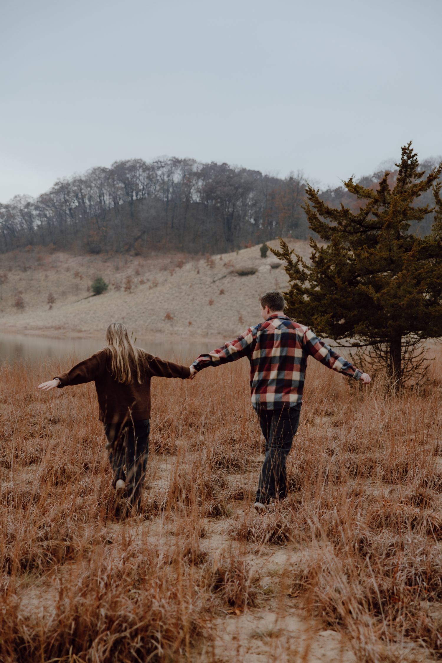 Two people walk hand in hand through a golden autumn hillside.