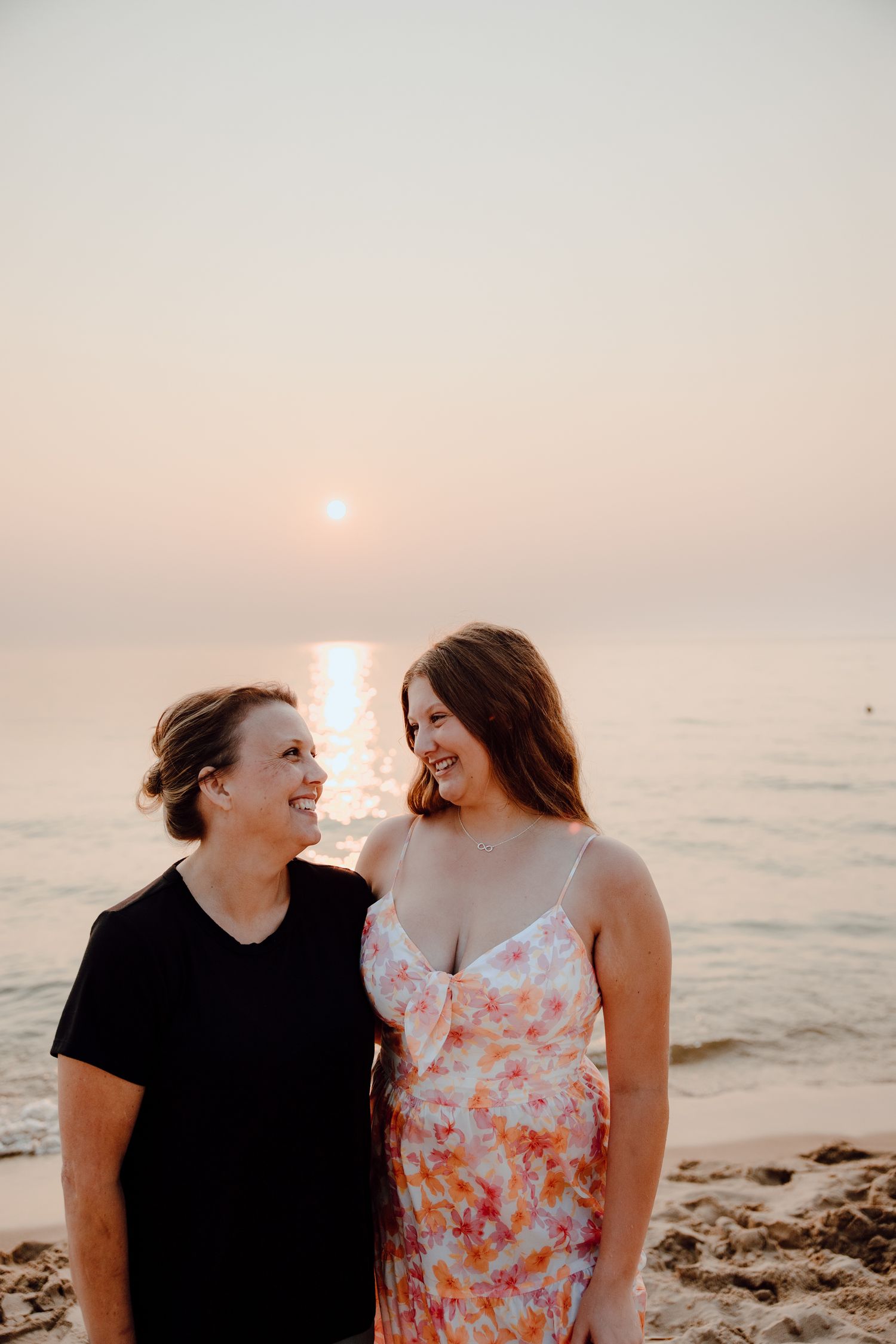 Two people share a tender moment on beach at sunset with ocean backdrop.