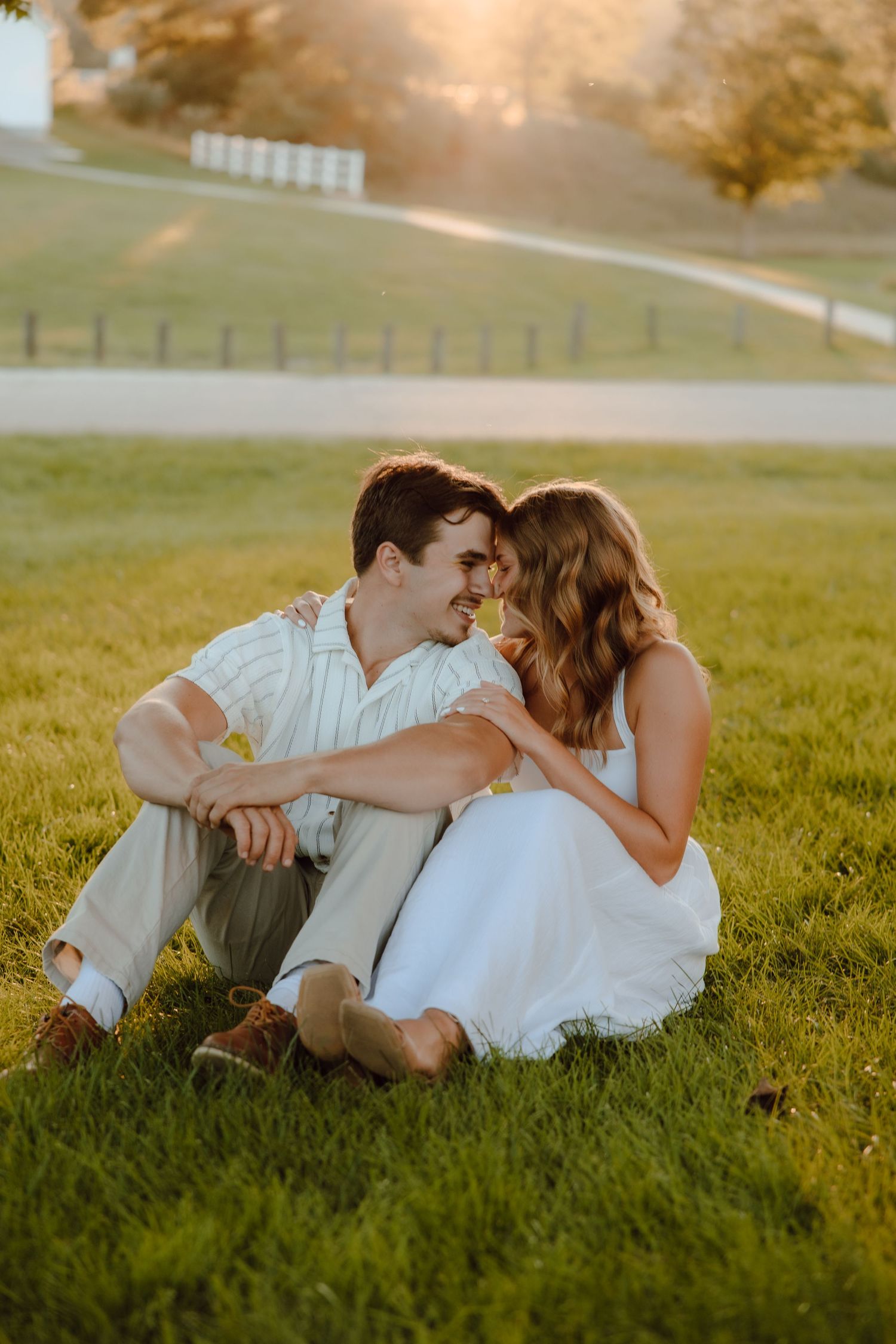 Couple sitting on green grass at golden hour, sharing a romantic moment at a countryside venue.