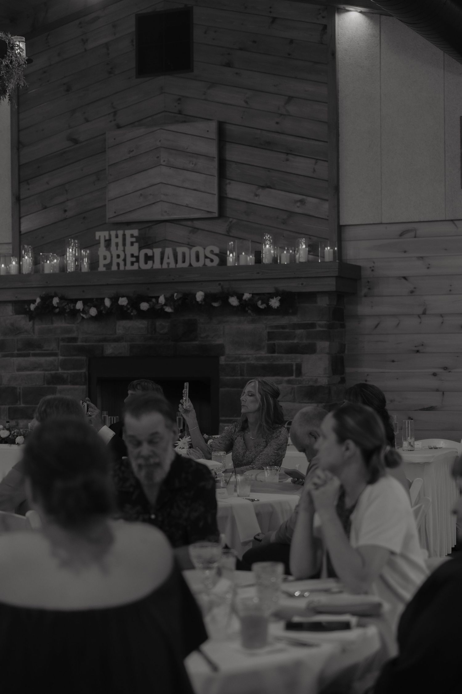 Wedding guests dining at The Preciados reception in a cozy rustic venue with stone fireplace.