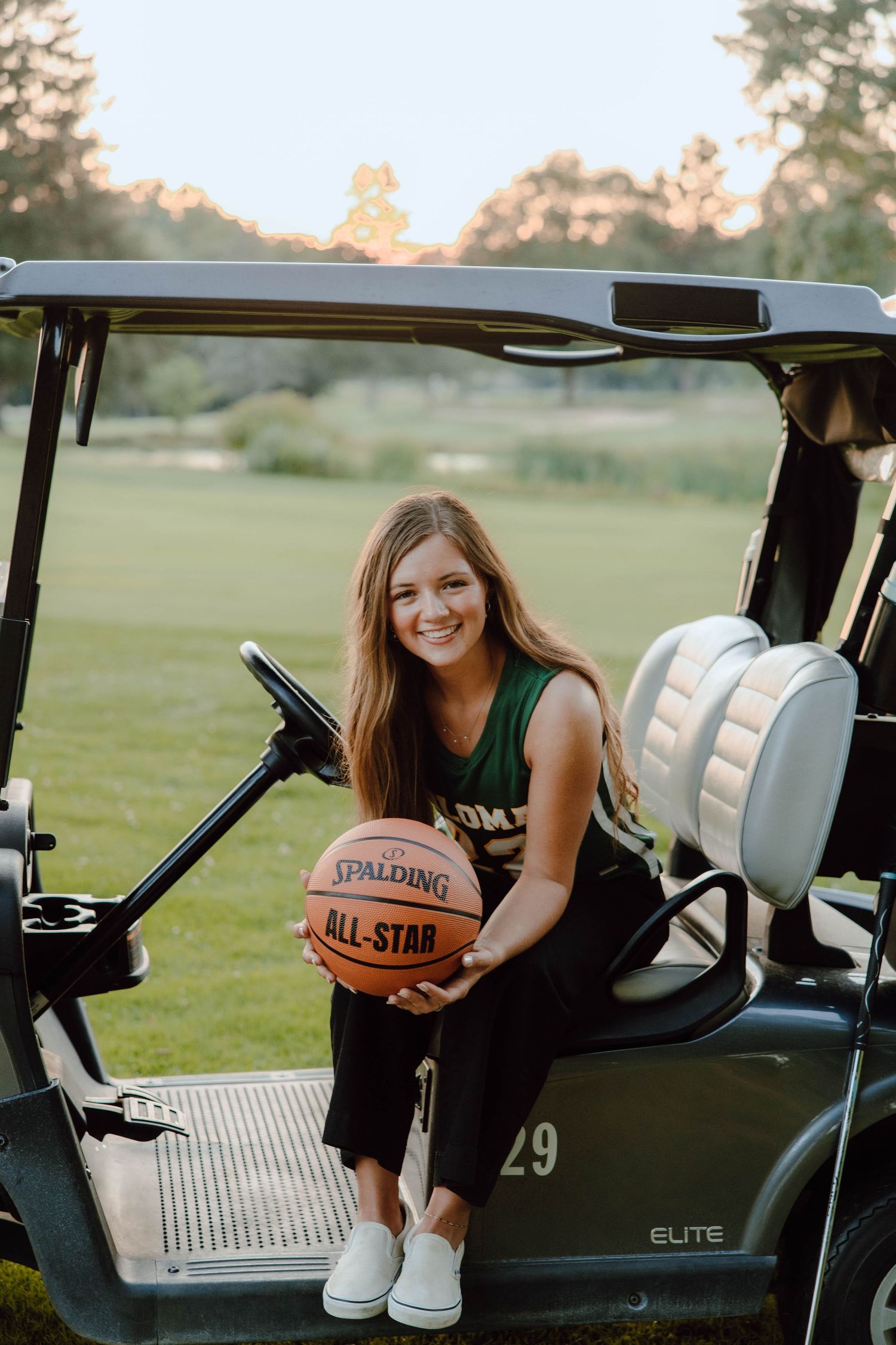 Young woman holding a Spalding All-Star basketball while sitting on a golf cart outdoors.
