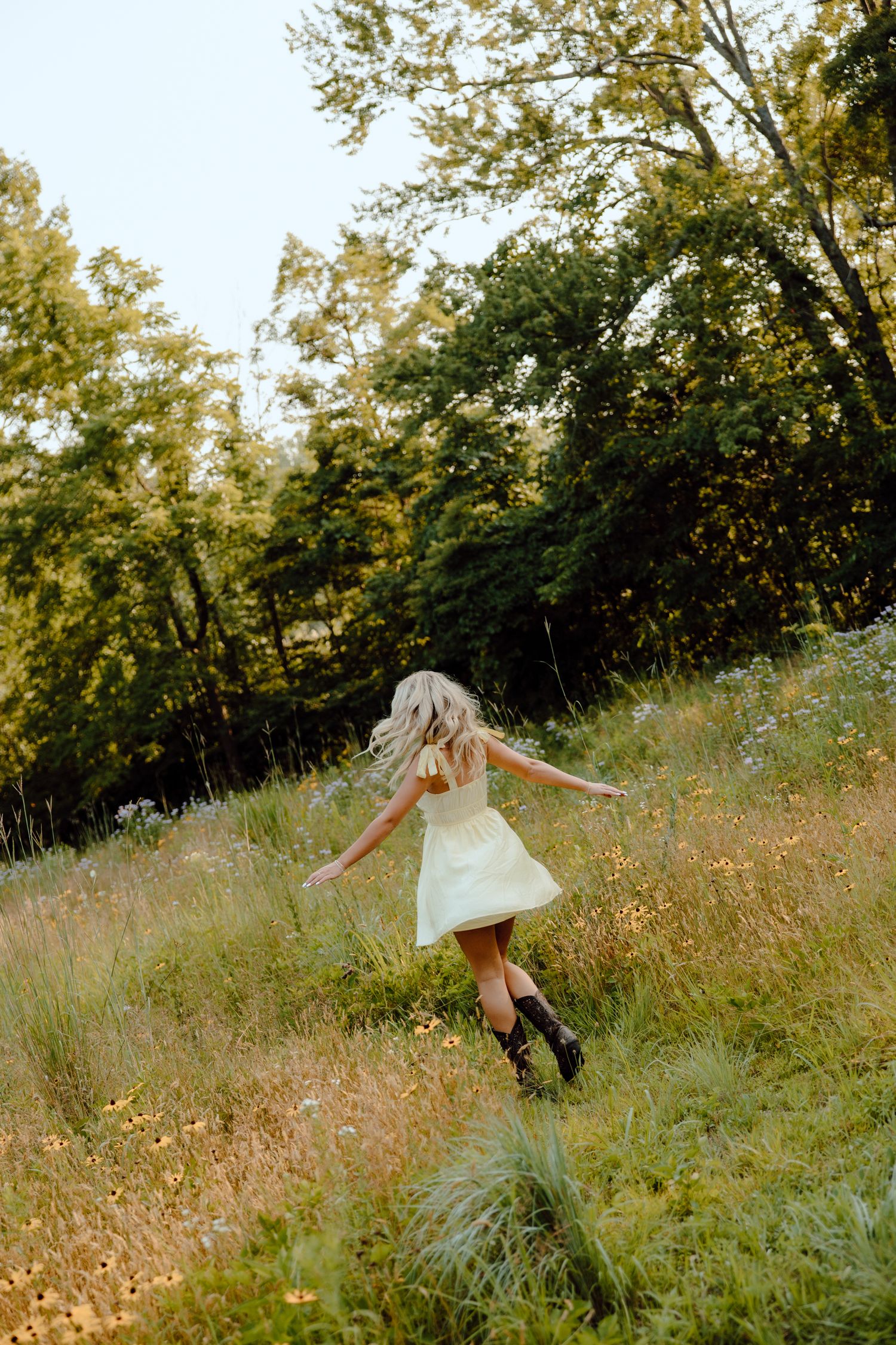 Carefree dancing through a wildflower meadow in a flowing white dress at sunset.