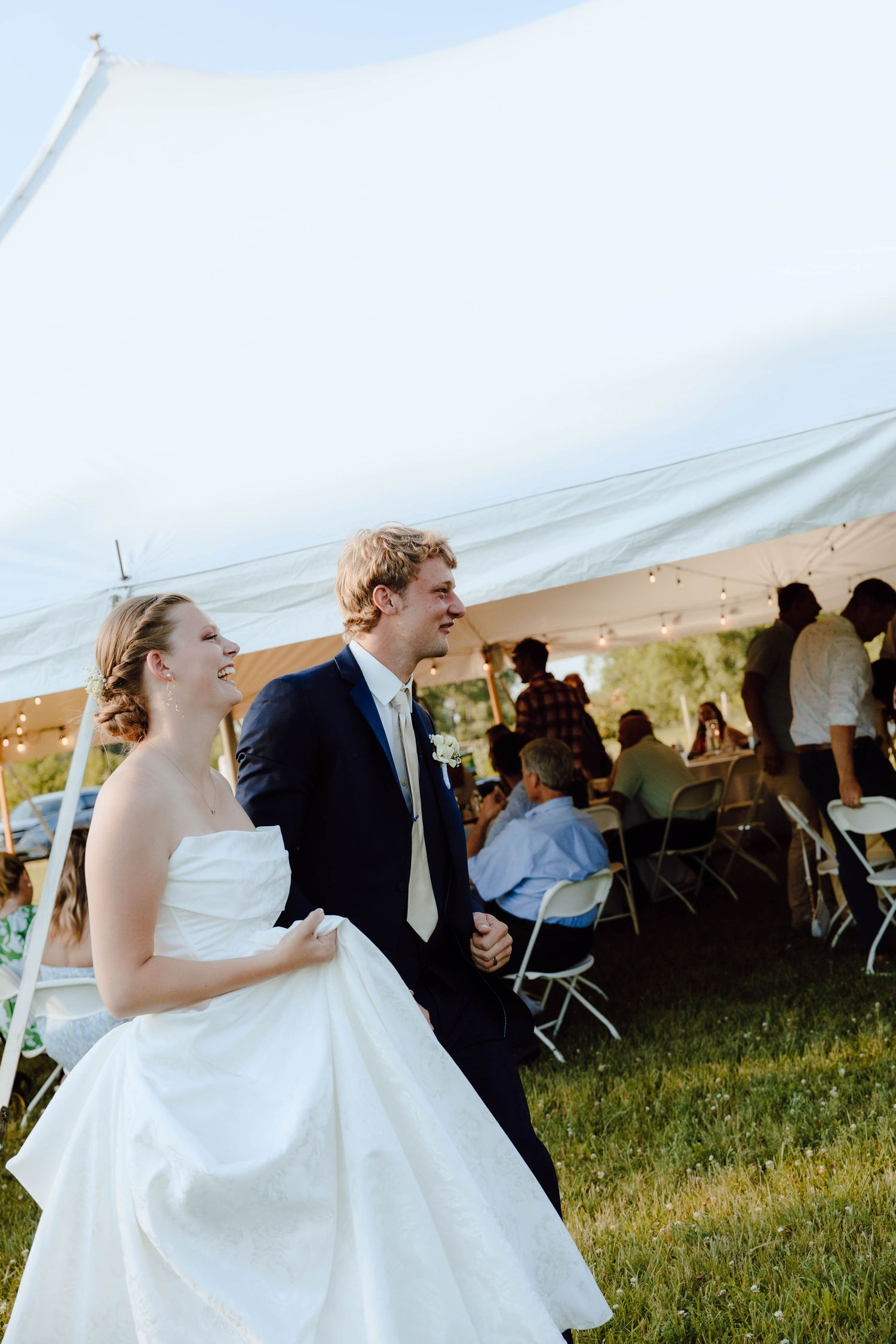 Newlyweds dance joyfully under a white tent during outdoor reception.