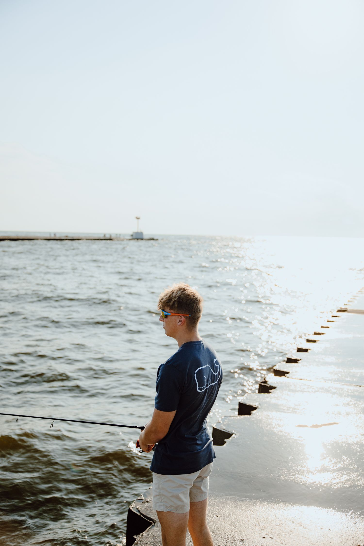 Person fishing along a pier at the beach during a sunny day.