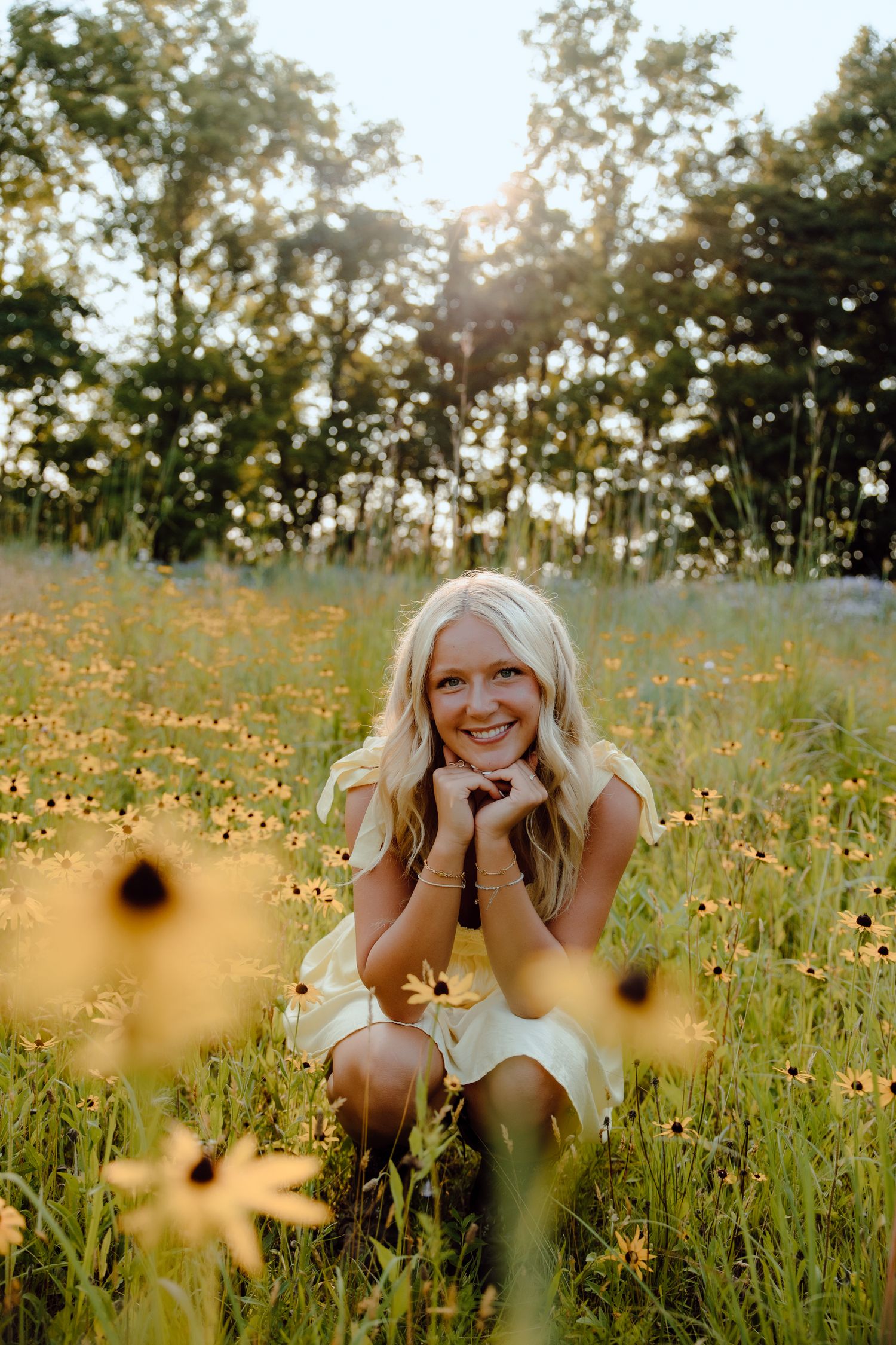 A dreamy summer portrait in a wildflower meadow at golden hour with yellow blooms and sunlit trees.