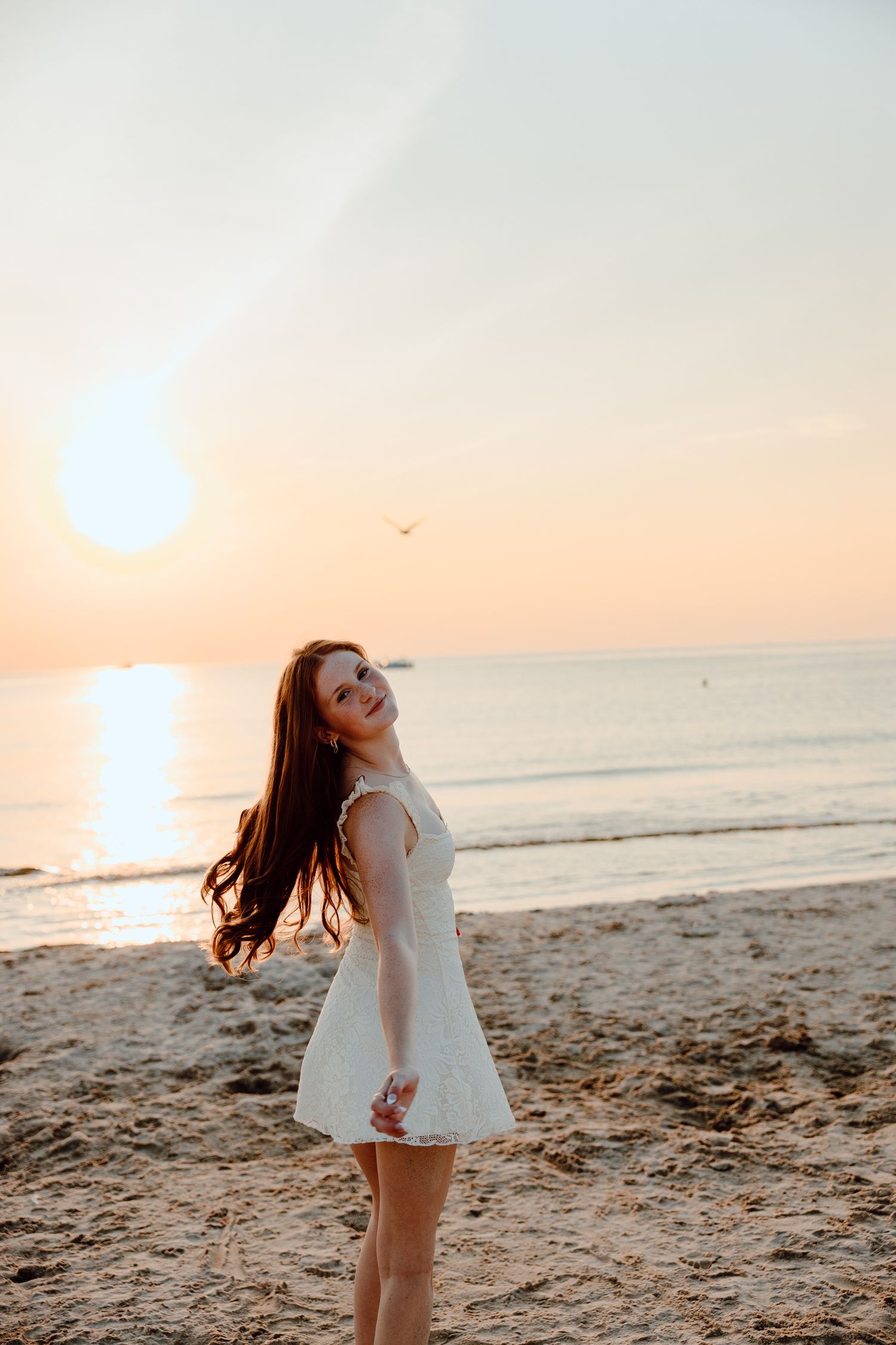 A dreamy beach photoshoot at sunset with a flowing white dress and windswept hair.