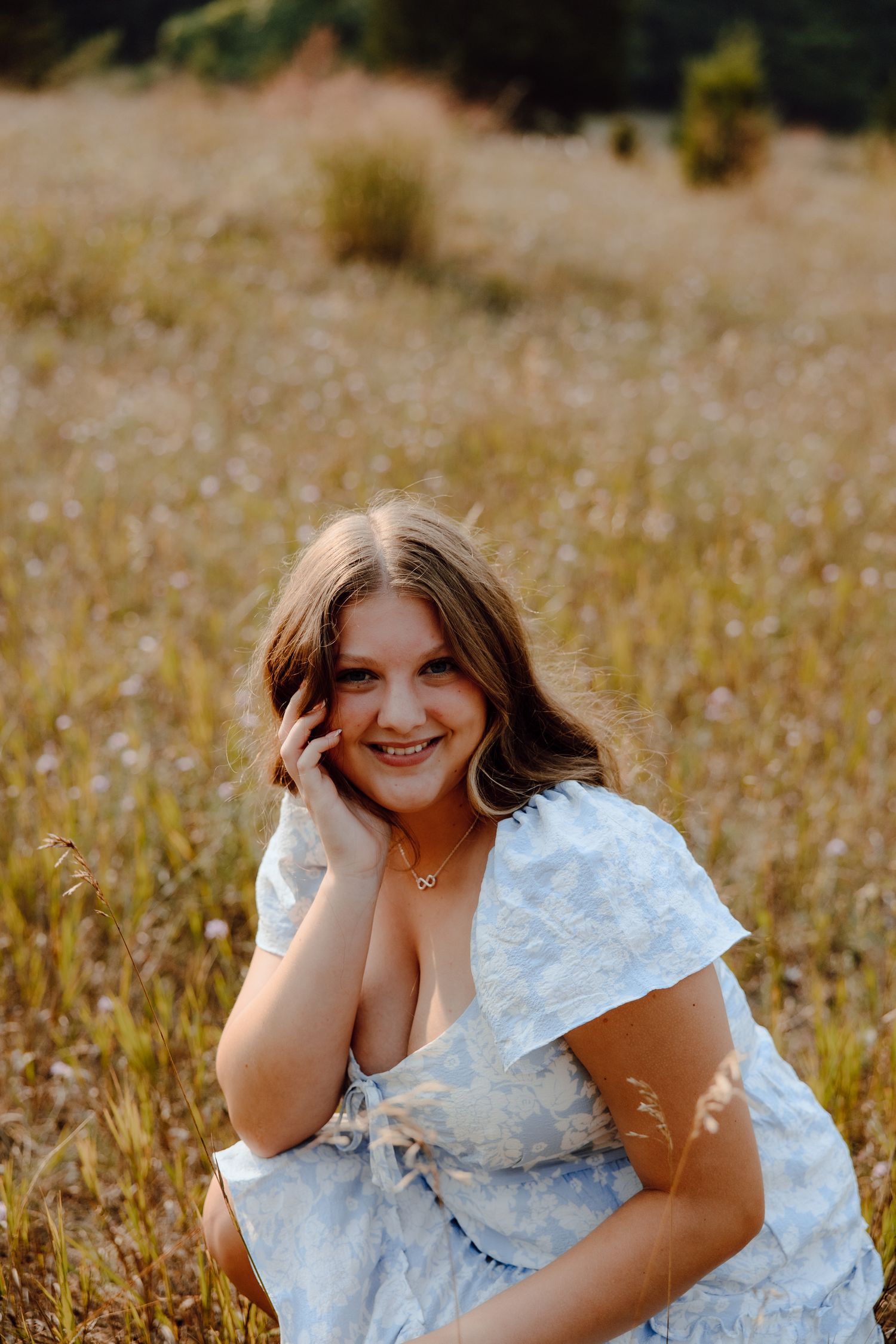 A person in a white dress poses cheerfully while sitting in a golden field.