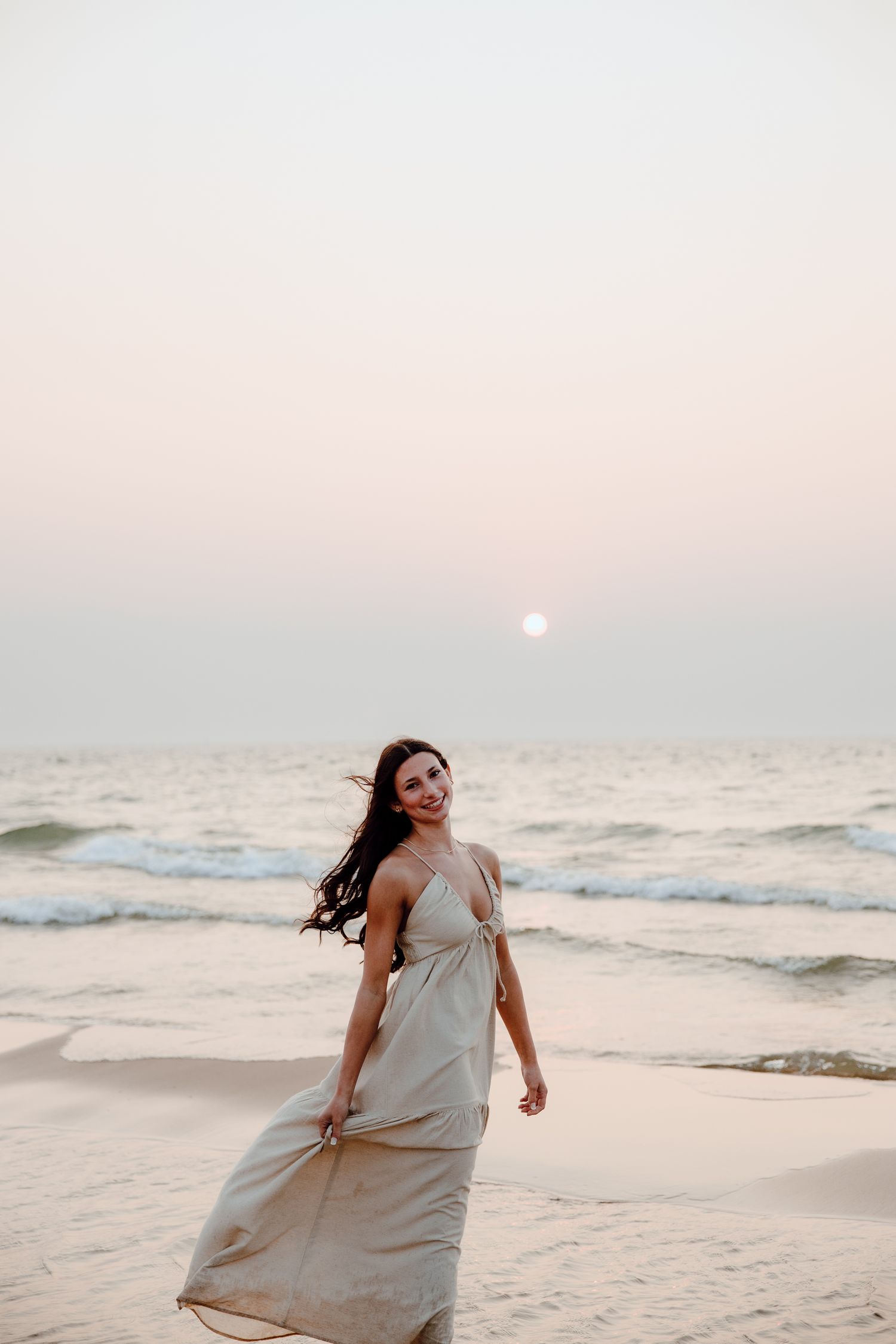 Woman in flowing dress dancing on beach at sunset with crashing waves.