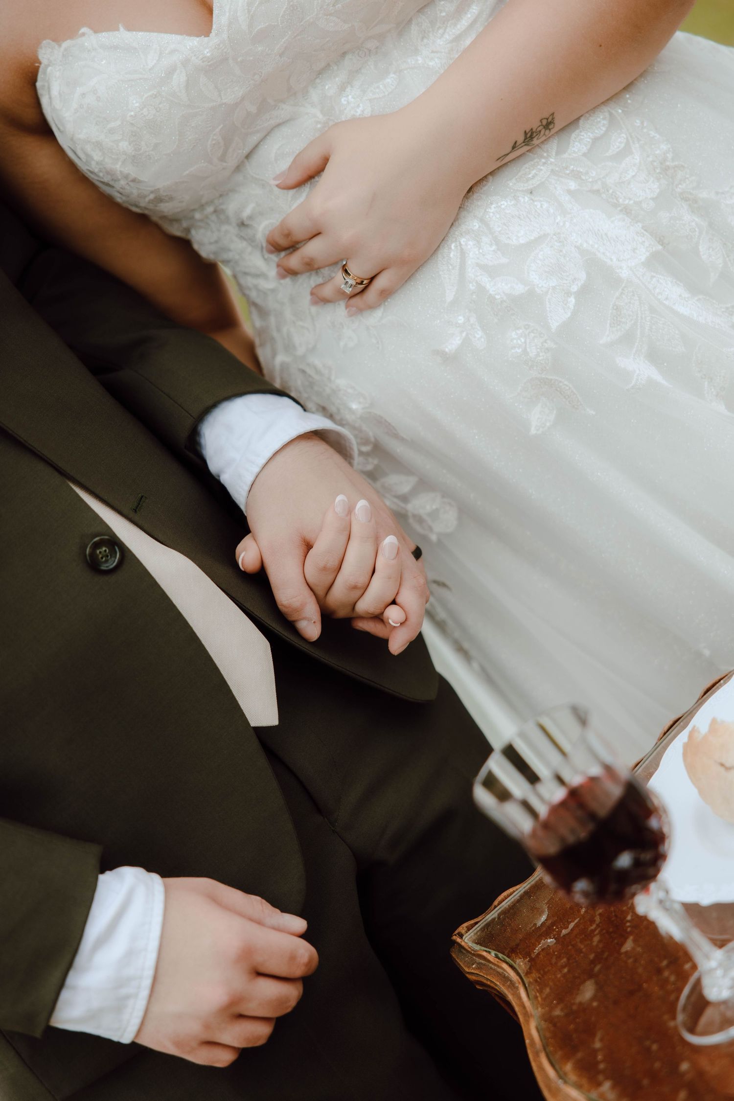 Bride and groom holding hands at wedding ceremony, bride wearing lace dress with gold ring, groom in dark suit.