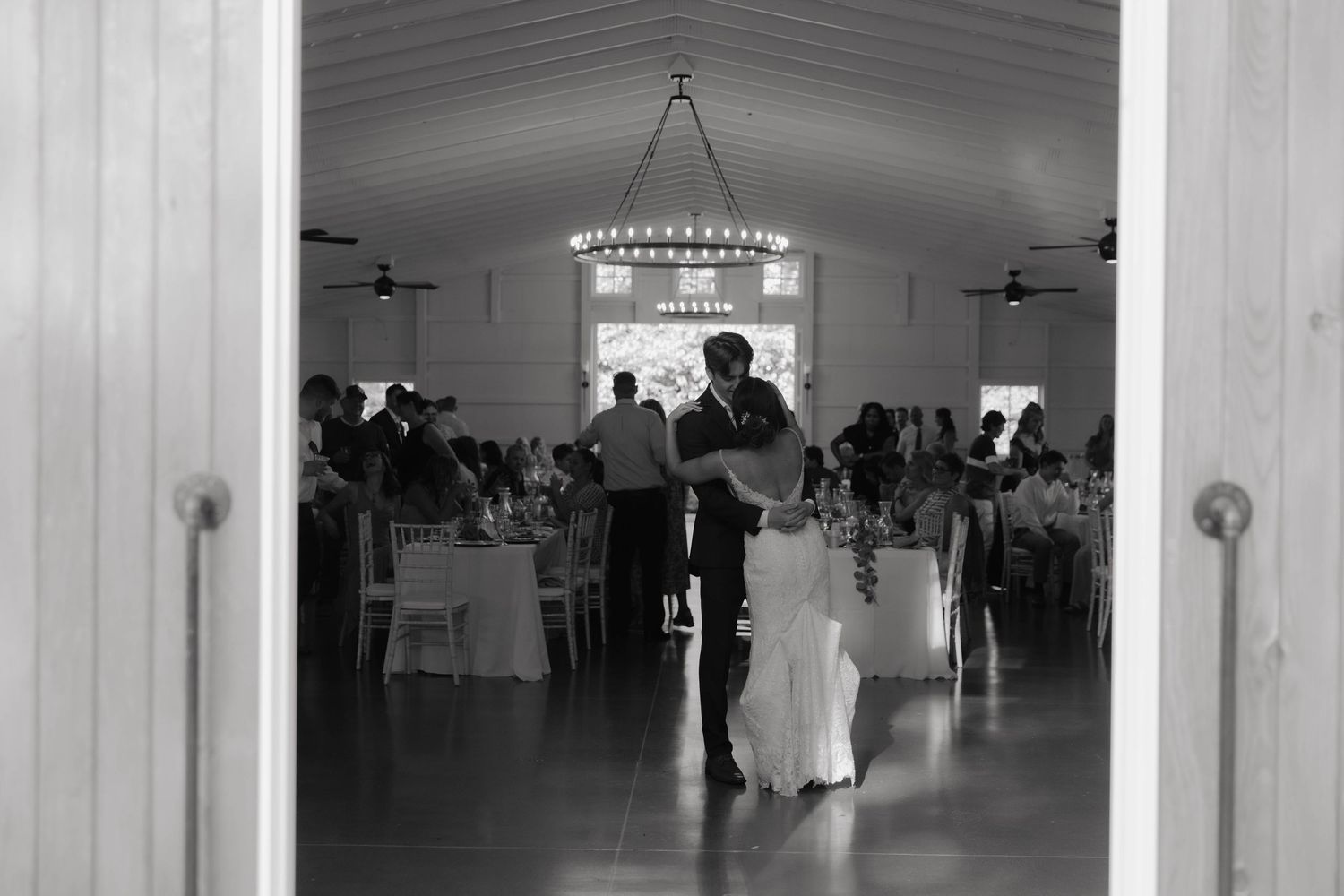 Black and white photo of a couple sharing their first dance at an elegant wedding reception in a barn venue.