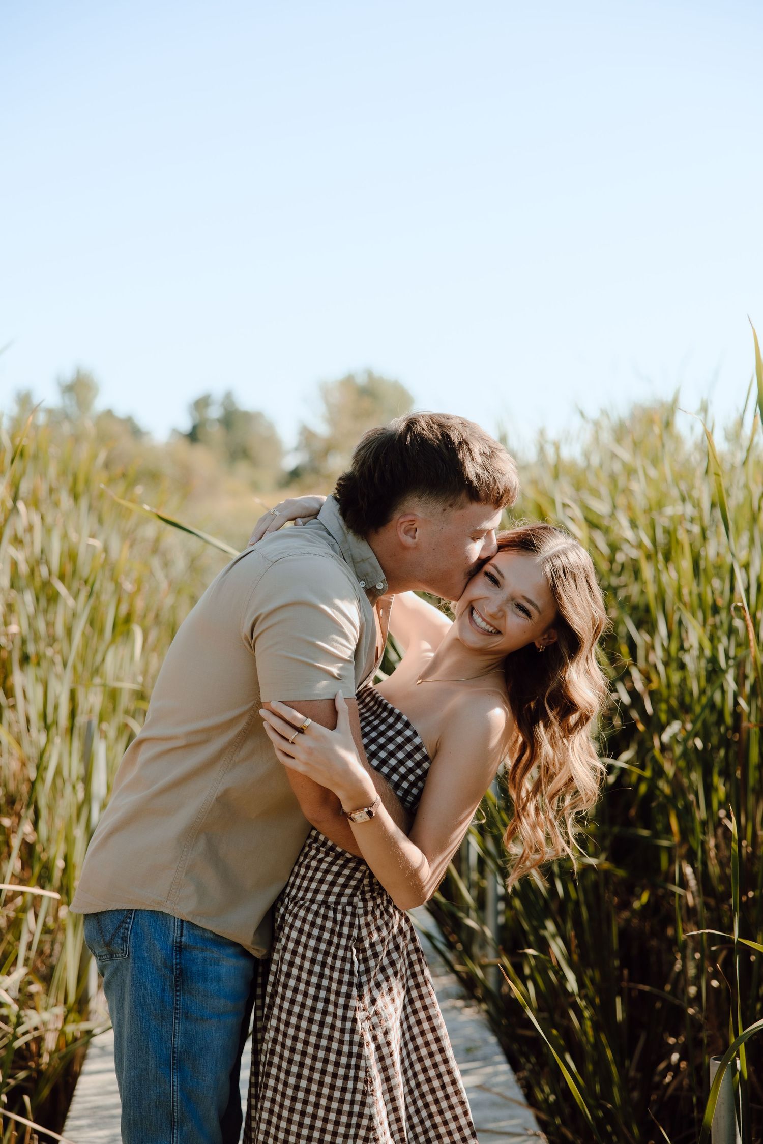 Happy couple embracing on a wooden dock surrounded by tall reeds on a sunny day.