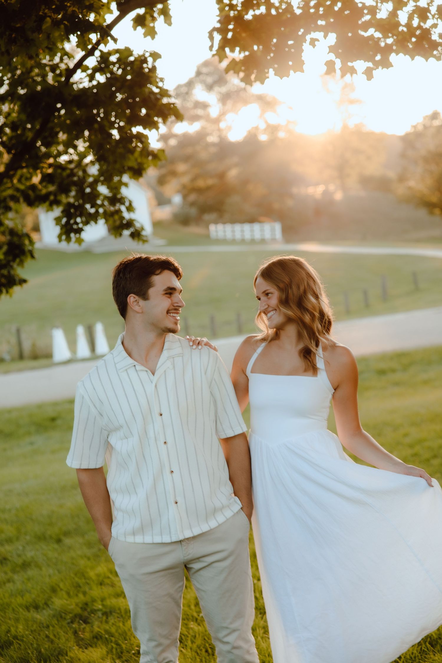 A couple smiles at each other during a golden hour outdoor photo session, woman in white dress.