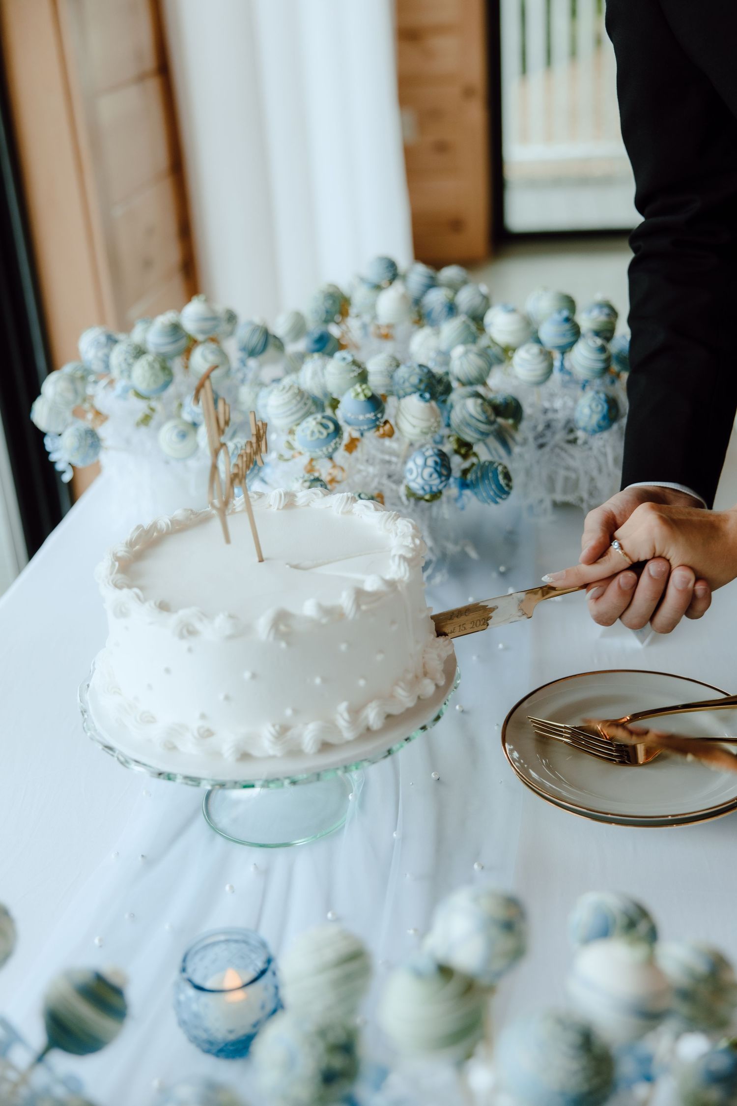 Bride and groom cutting white wedding cake surrounded by blue cake pops.