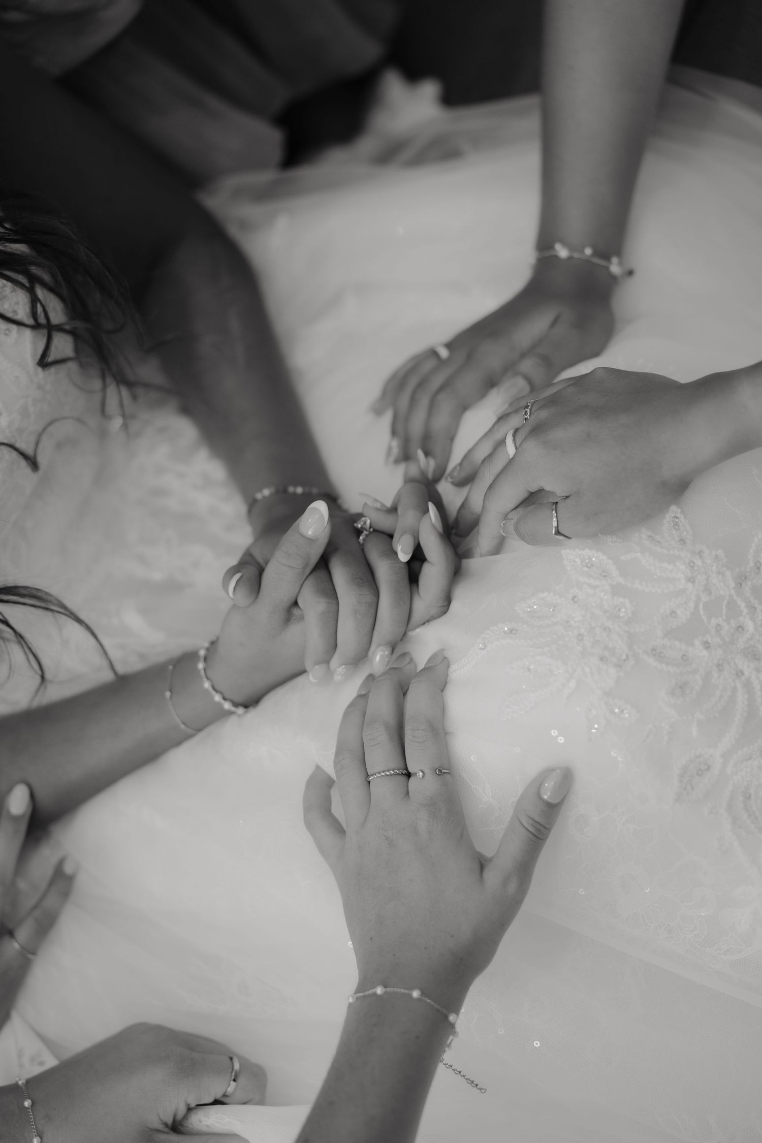 Black and white photo of bridesmaids placing hands together over brides white wedding gown.