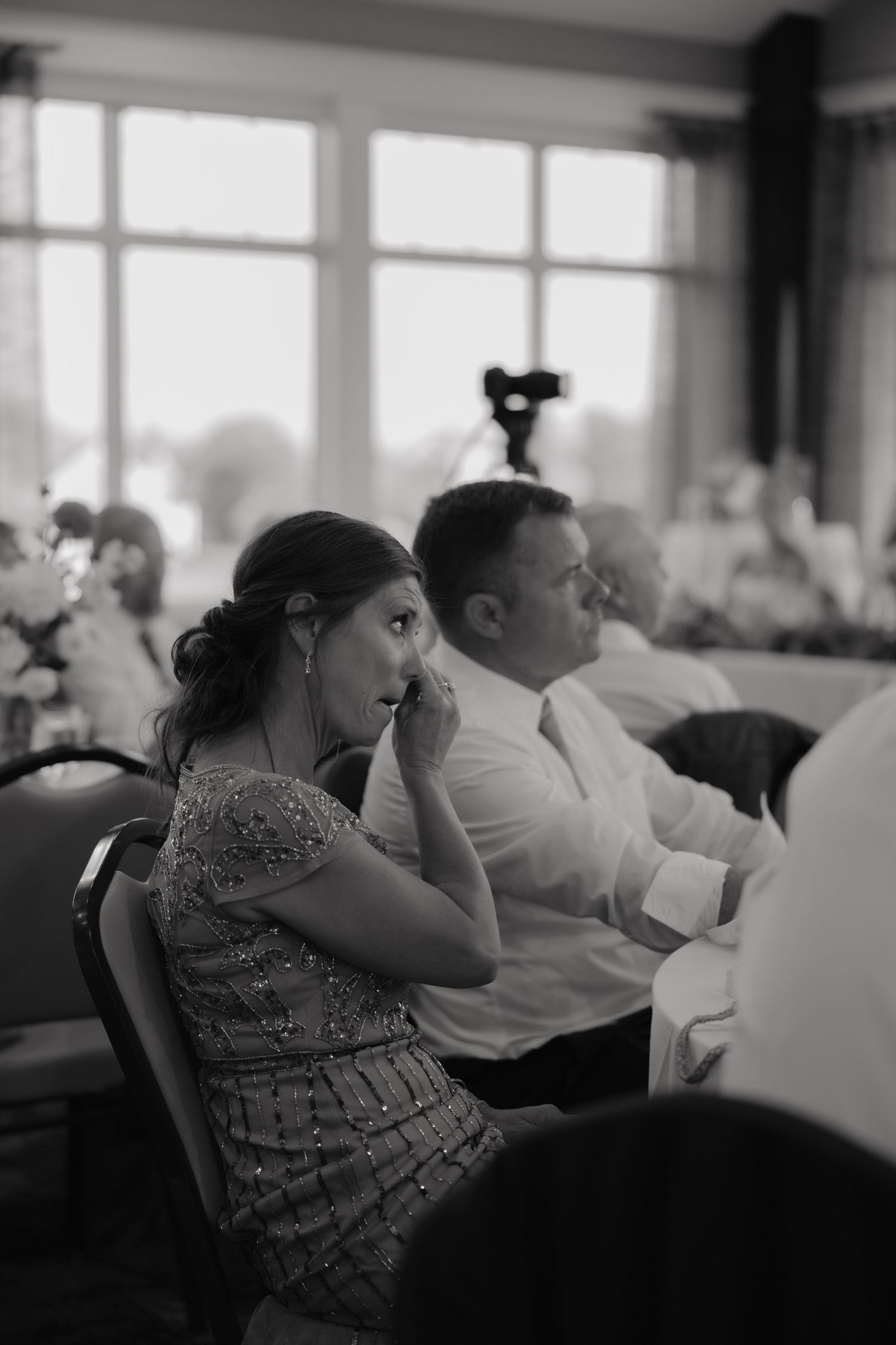 Emotional wedding guest wiping tears during ceremony in black and white photo.
