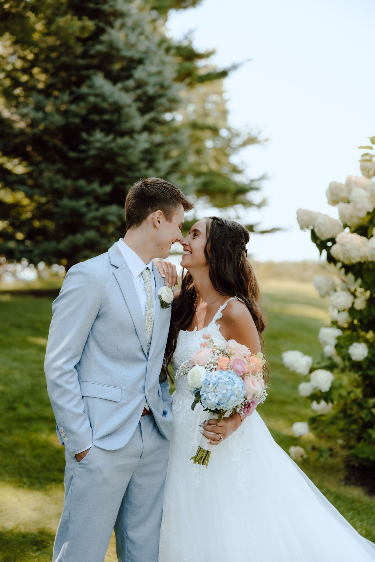Bride and groom share a romantic moment outdoors near a floral arch, bride holding a pastel bouquet.