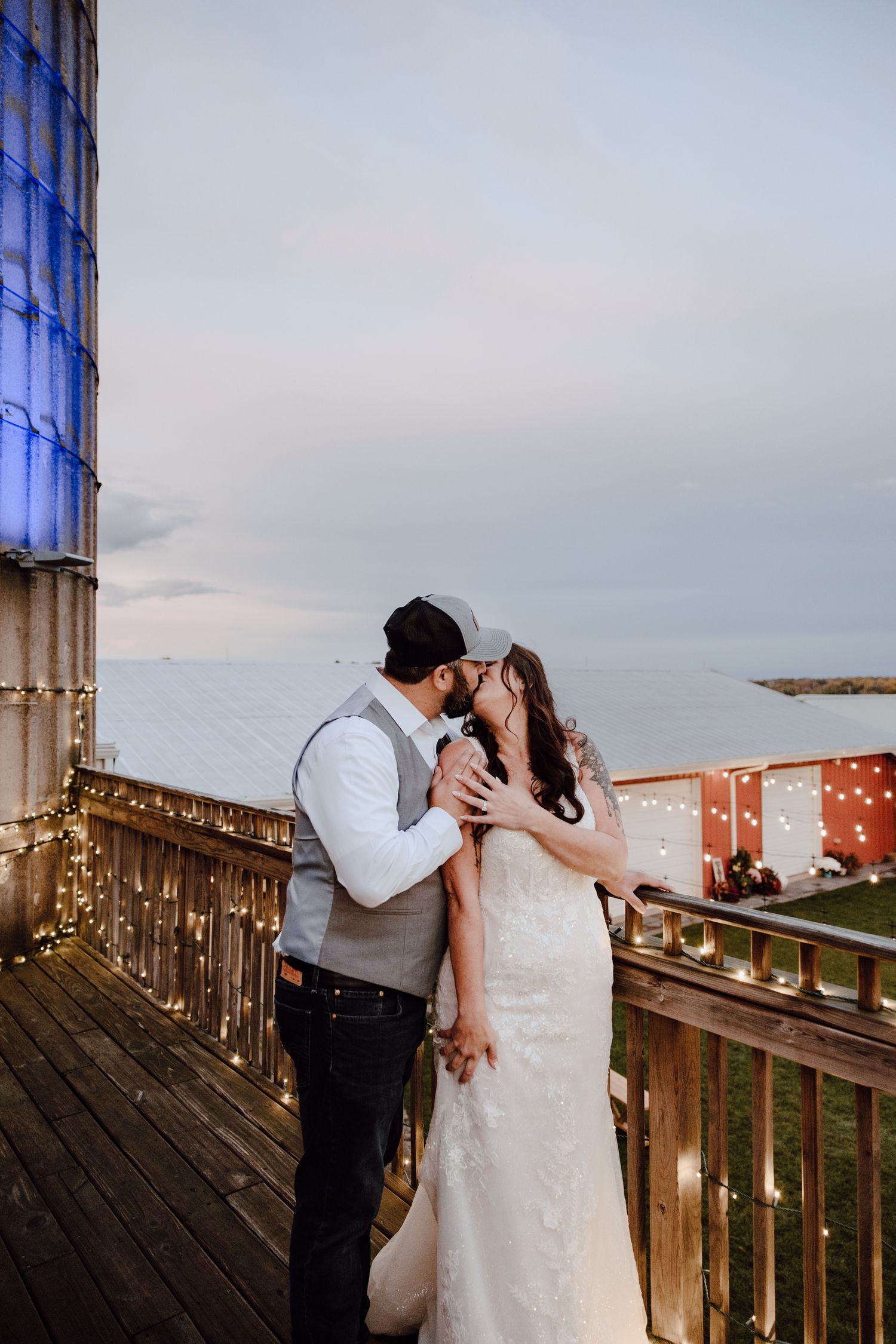 A couple shares a romantic moment on a wooden deck decorated with string lights at sunset.