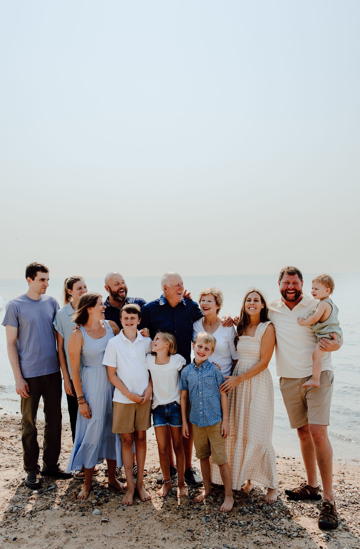 A large extended family poses together on a beach during a casual photo session.
